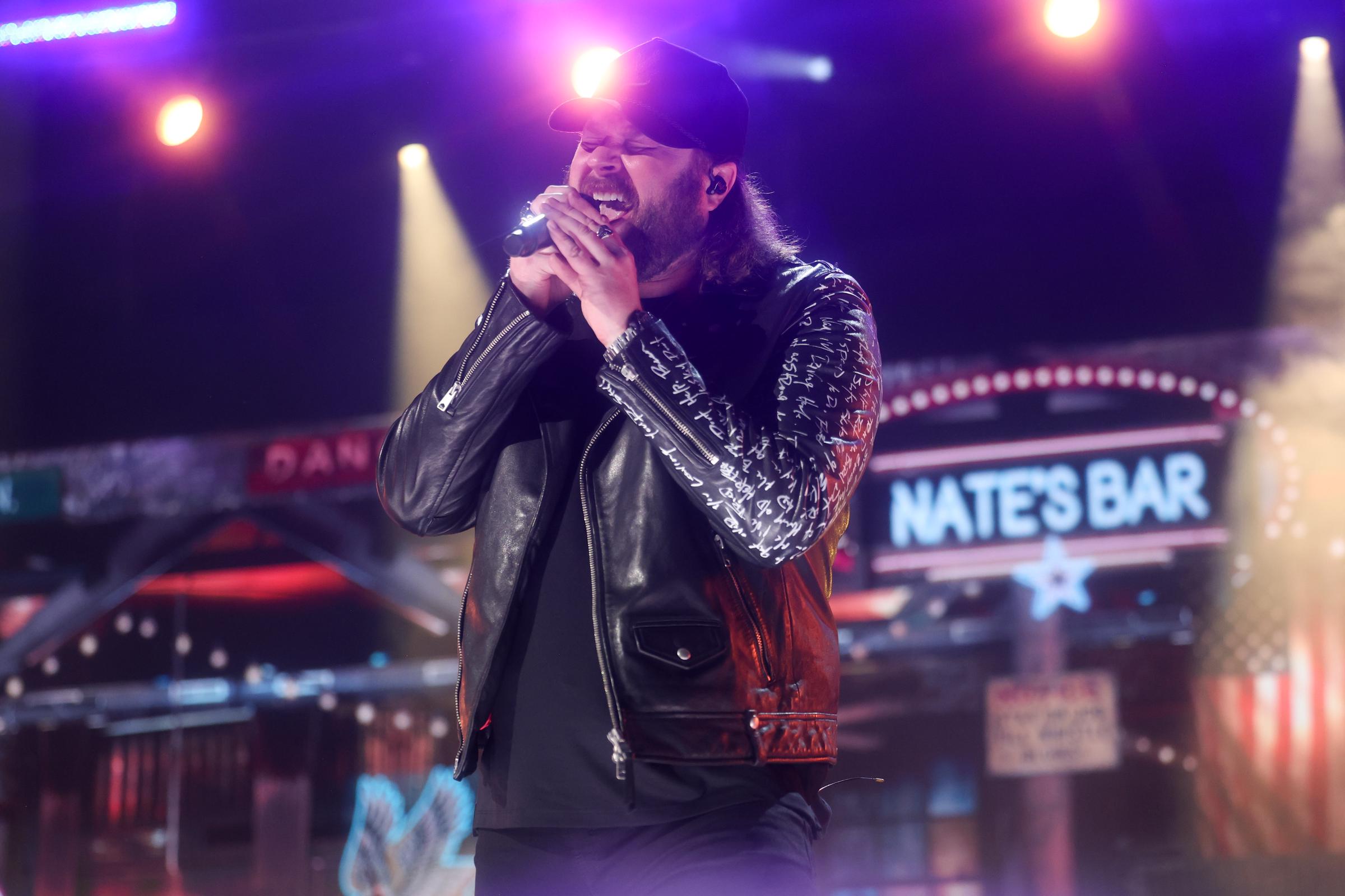 Nate Smith belts into the microphone with his eyes closed, gripping it with both hands as colorful stage lights frame the intensity of his performance.