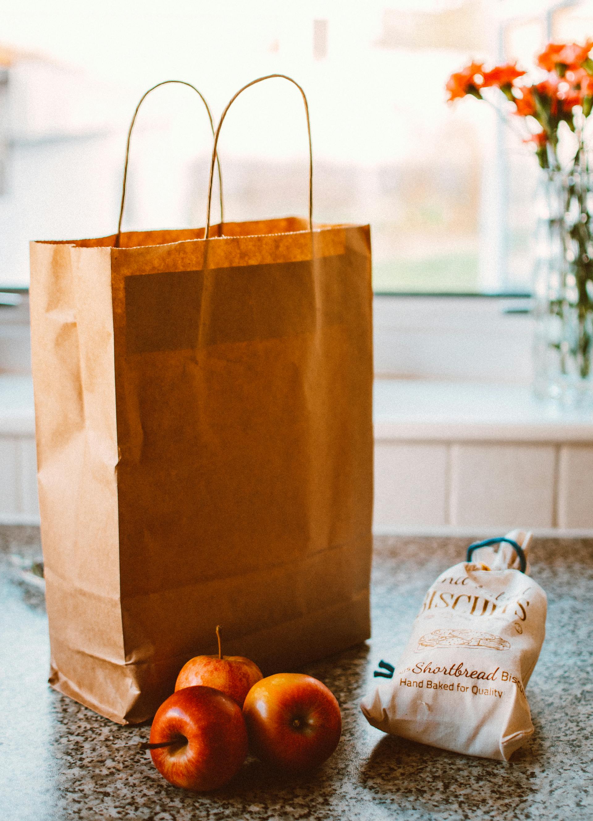 Several apples lying beside a brown paper bag and a pack of bread | Source: Pexels