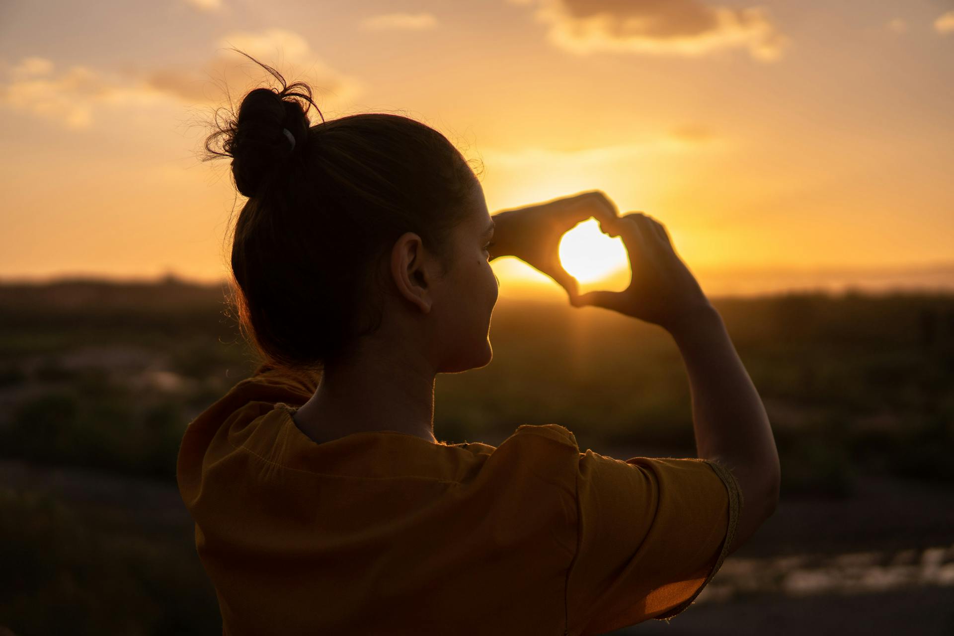 A back view shot of a woman making a heart sign with her hands during golden hour | Source: Pexels