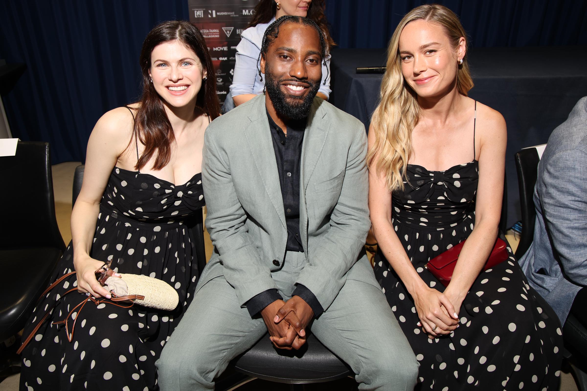 Alexandra Daddario and Brie Larson pose with John David Washington between them as they attend the Filming Italy press conference on June 20, 2024, in Cagliari, Italy. Both actresses wear the same black-and-white polka dot Dôen “Maryanna” dress, creating a chic twinning moment.