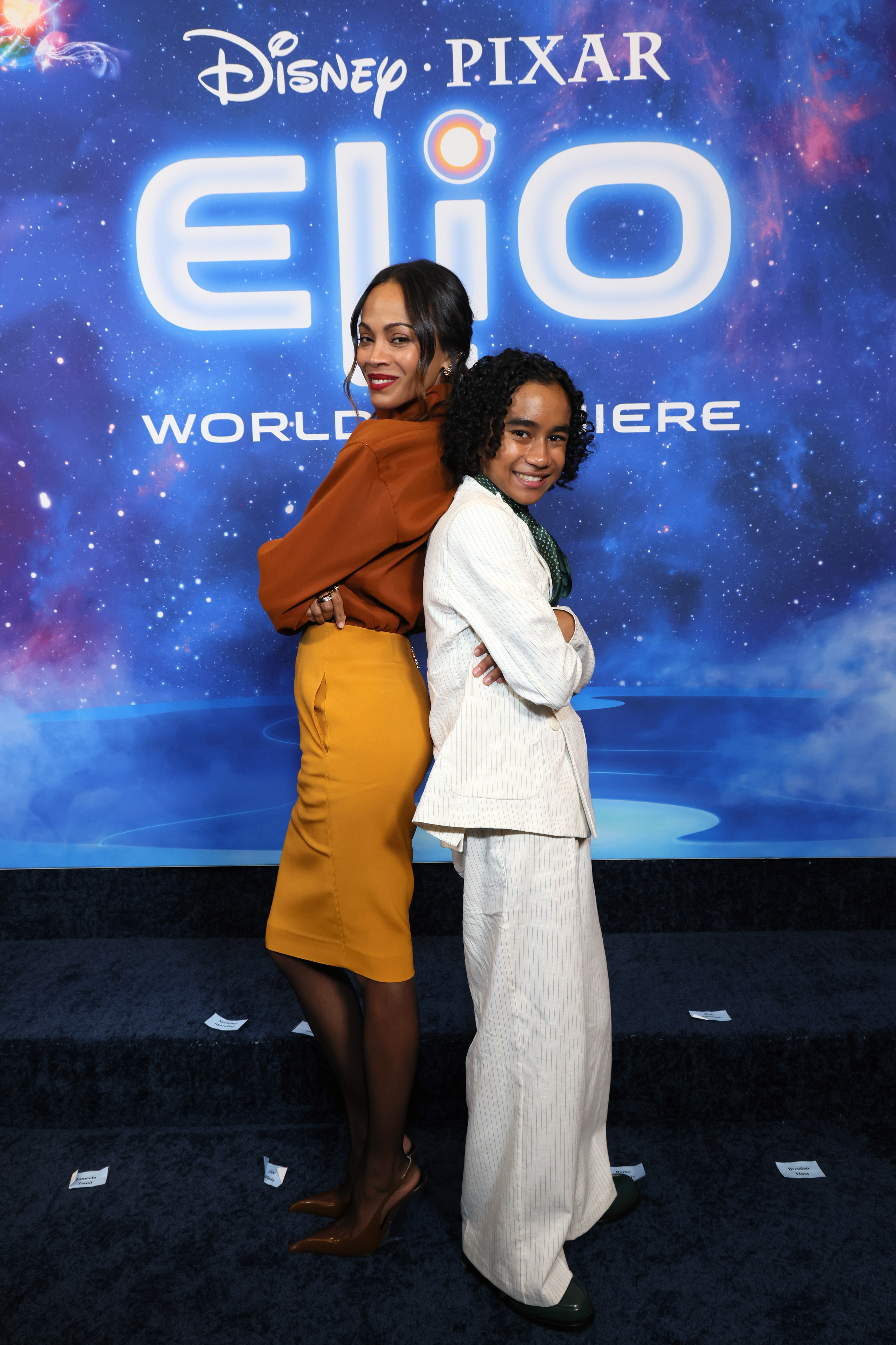 Zoe Saldaña smiling and showing her playful side as she photographs in a back-to-back pose with Yonas Kibreab.