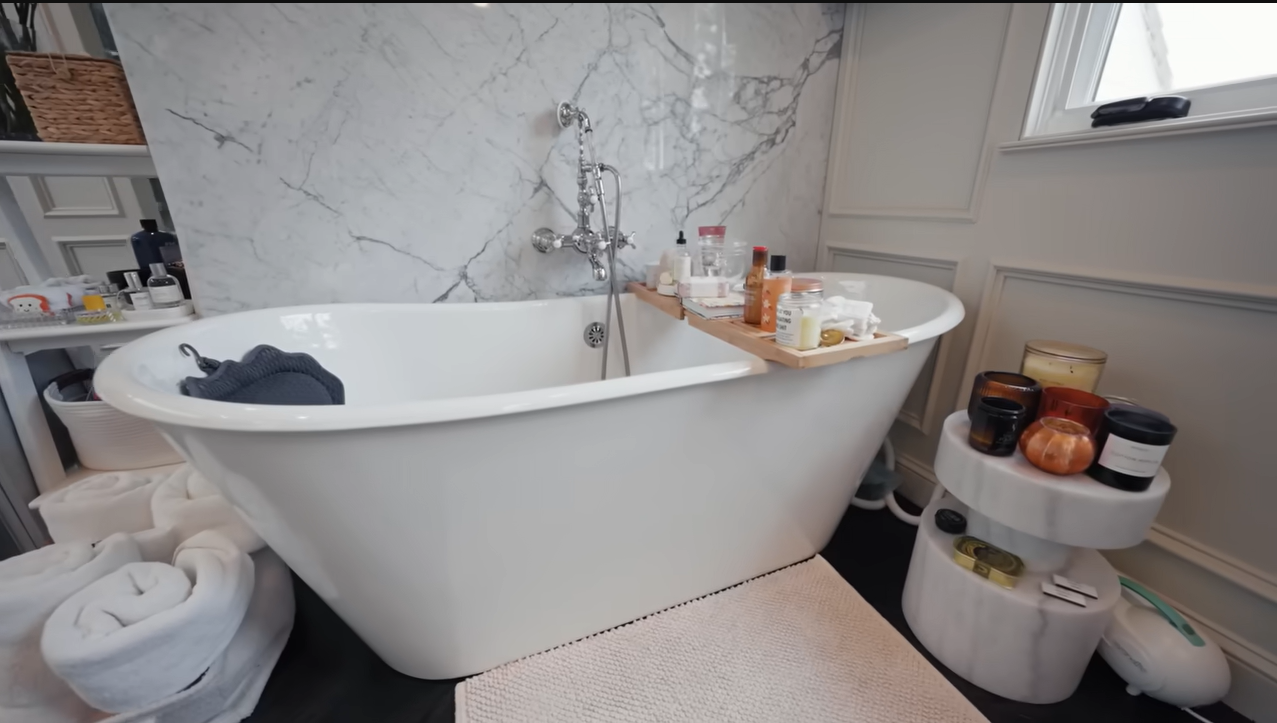 Palmer's standalone tub is fully stocked with endless candles, face masks, and a handy wooden caddy tray.  | Source: YouTube/@Archdigest