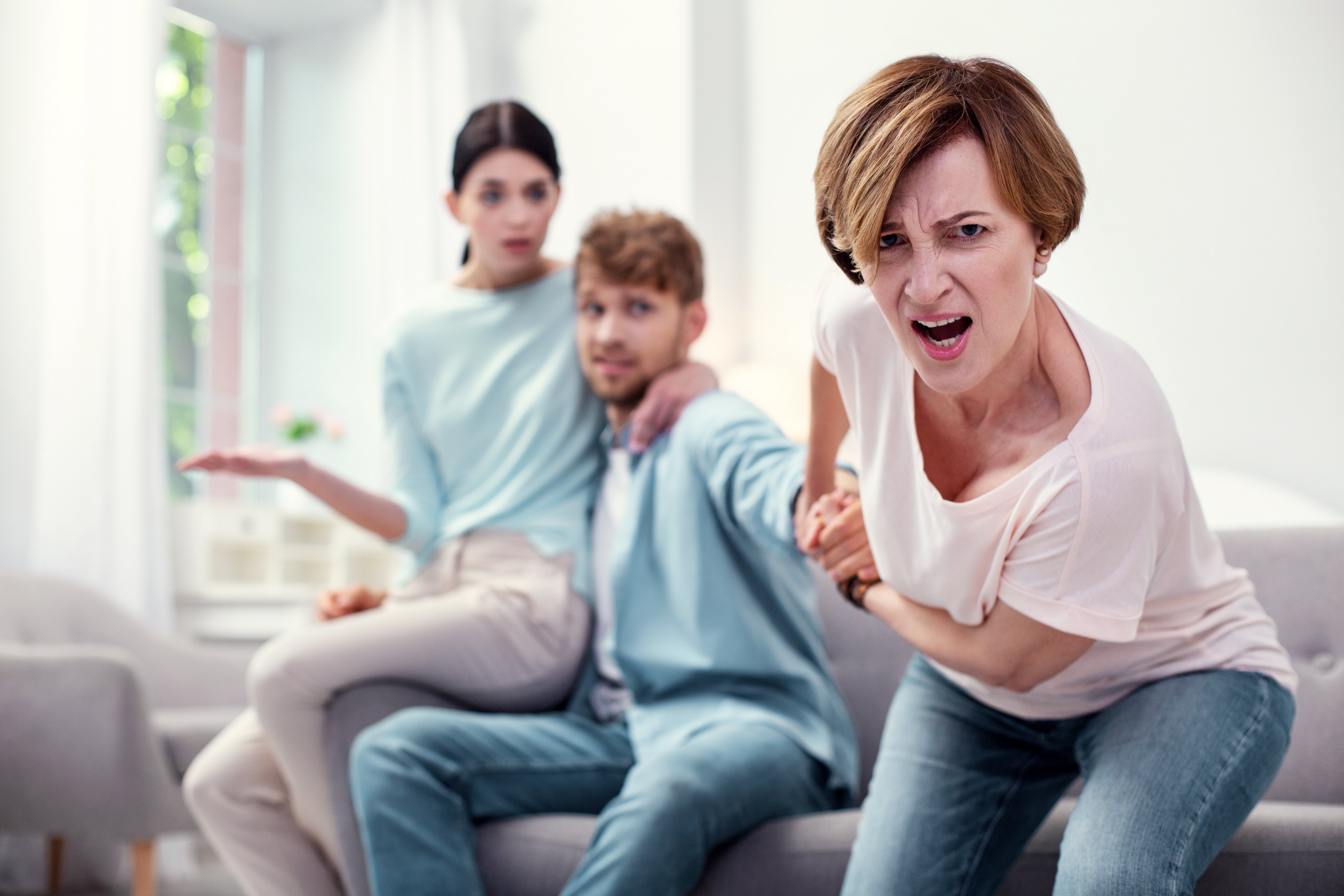 Angry woman dragging son while younger woman sits next to him. | Source: Shutterstock