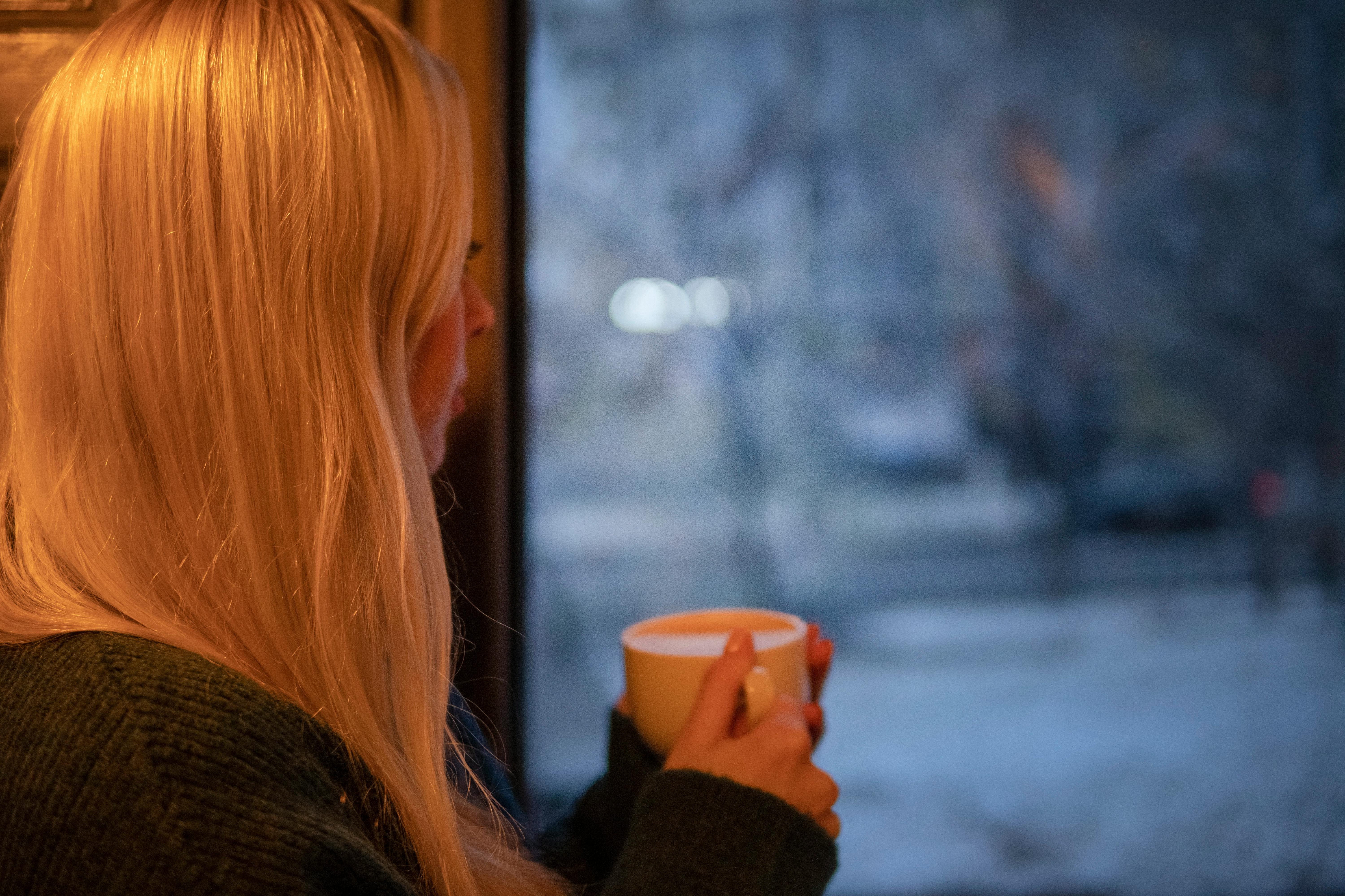 A girl with a coffee cup looking out the window | Source: Pexels