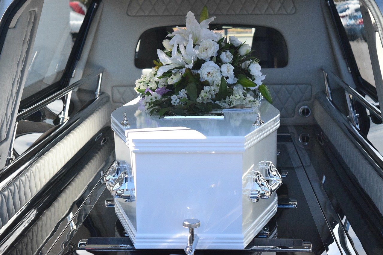 A coffin with flowers on top, placed inside the back of a hearse | Photo: Pixabay/Carolyn Booth