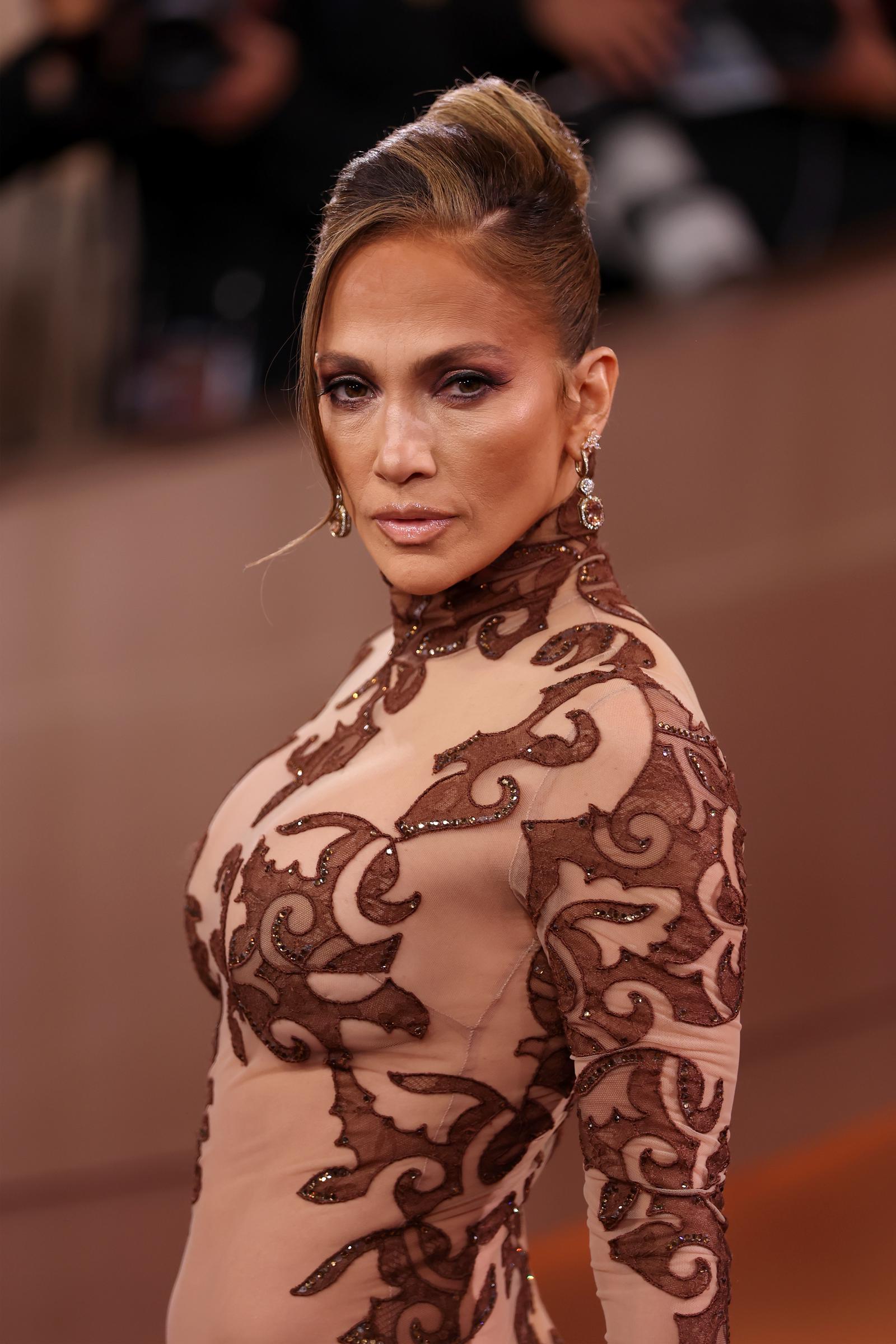 Jennifer Lopez holds a fierce gaze while pausing mid-turn on the carpet, her earrings catching the light as she faces the press line | Source: Getty Images