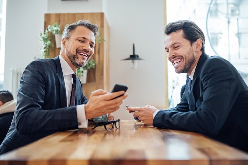 Photo of two businessmen sitting at coffee shop using mobile phone | Photo: Getty Images