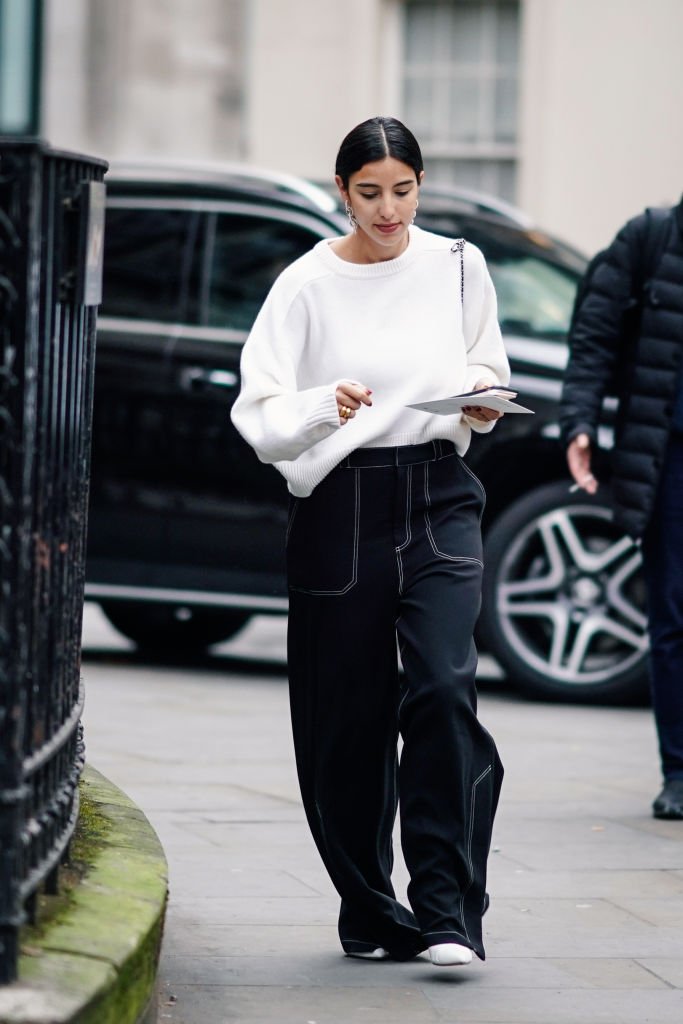 Ein Gast trägt Ohrringe, einen weißen Pullover, dunkelblaue Baggy-Jeans und weiße Schuhe während der London Fashion Week im Februar 2019 am 18. Februar 2019 in London, England | Quelle: Getty Images