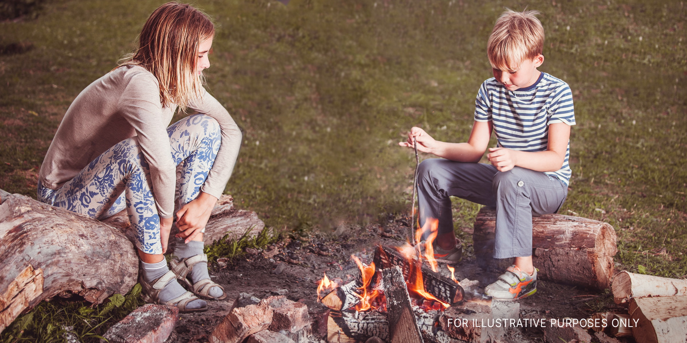 A boy and girl sit across from each other at a campfire | Source: Shutterstock