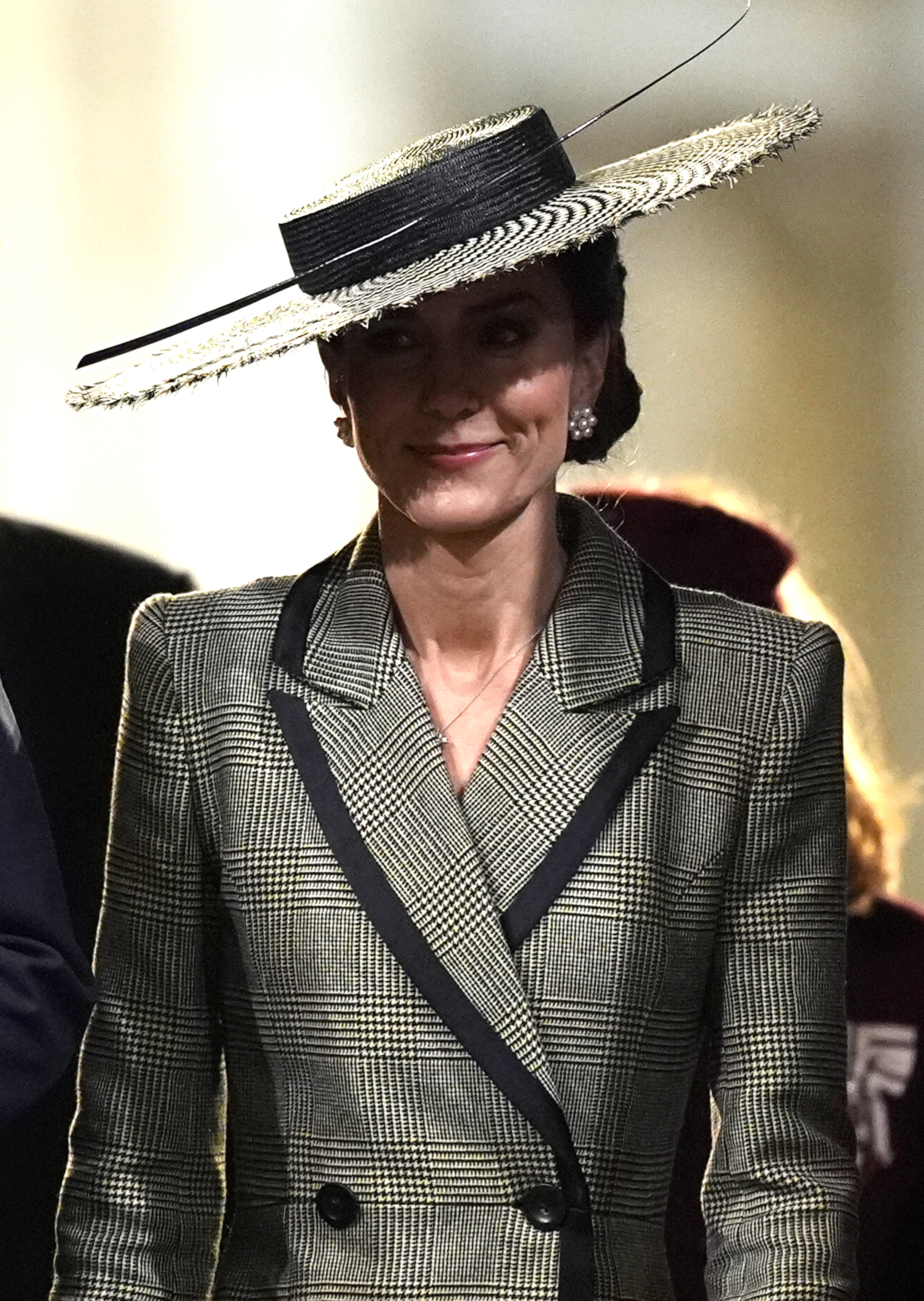 Inside the cathedral, the wind has been defeated and composure fully restored. Cameras capture the Princess of Wales with a calm, composed expression, the boater hat sitting perfectly level now that it no longer had the Canterbury gusts to contend with. The sharp black lapels of the Suzannah London coatdress frame the delicate diamond cross necklace at her throat, and the pearl cluster earrings are clearly visible against her pinned-back hair.