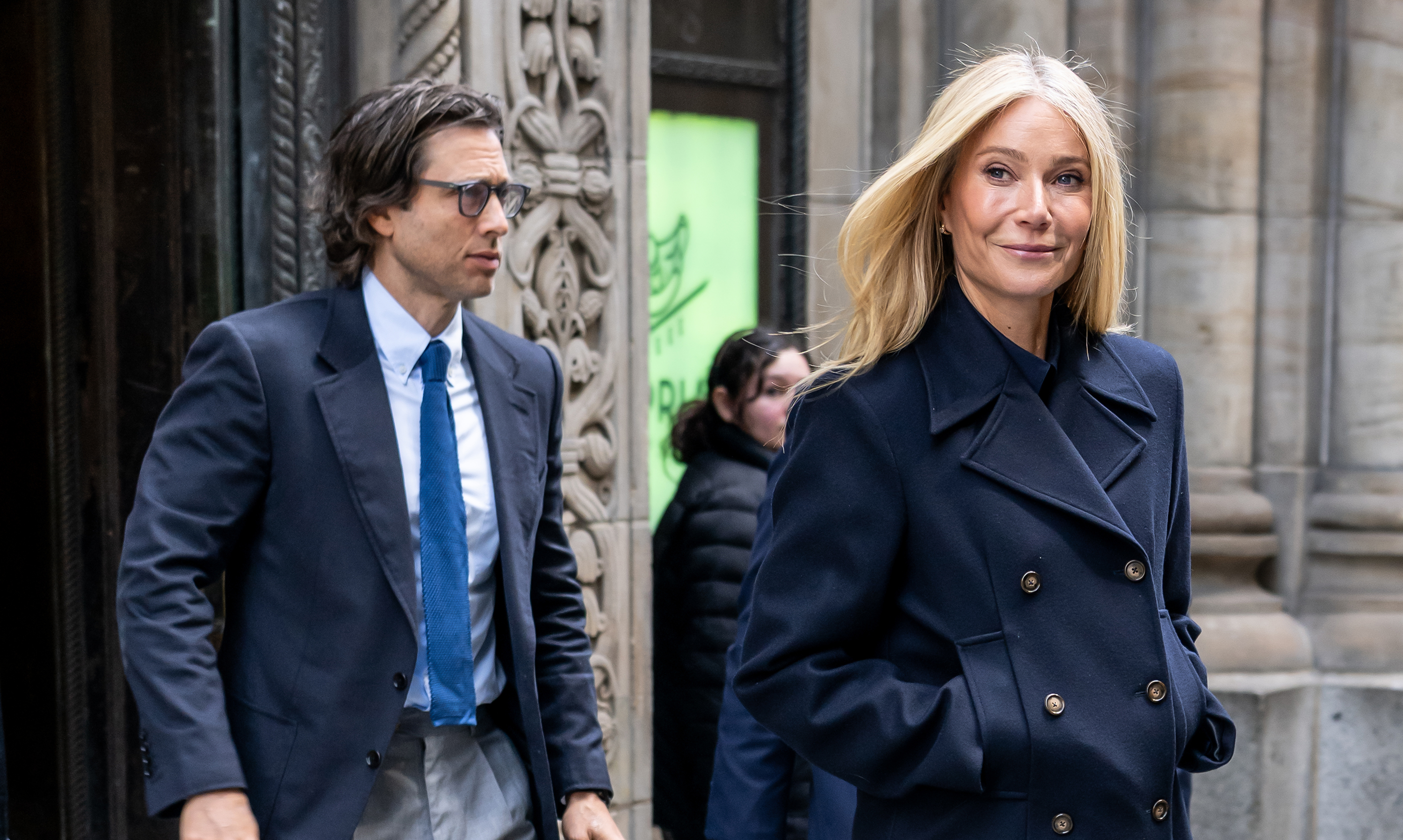 Gwyneth Paltrow glances to the side while walking past a building in New York City, her expression relaxed as Brad Falchuk follows just behind her in a navy suit.
