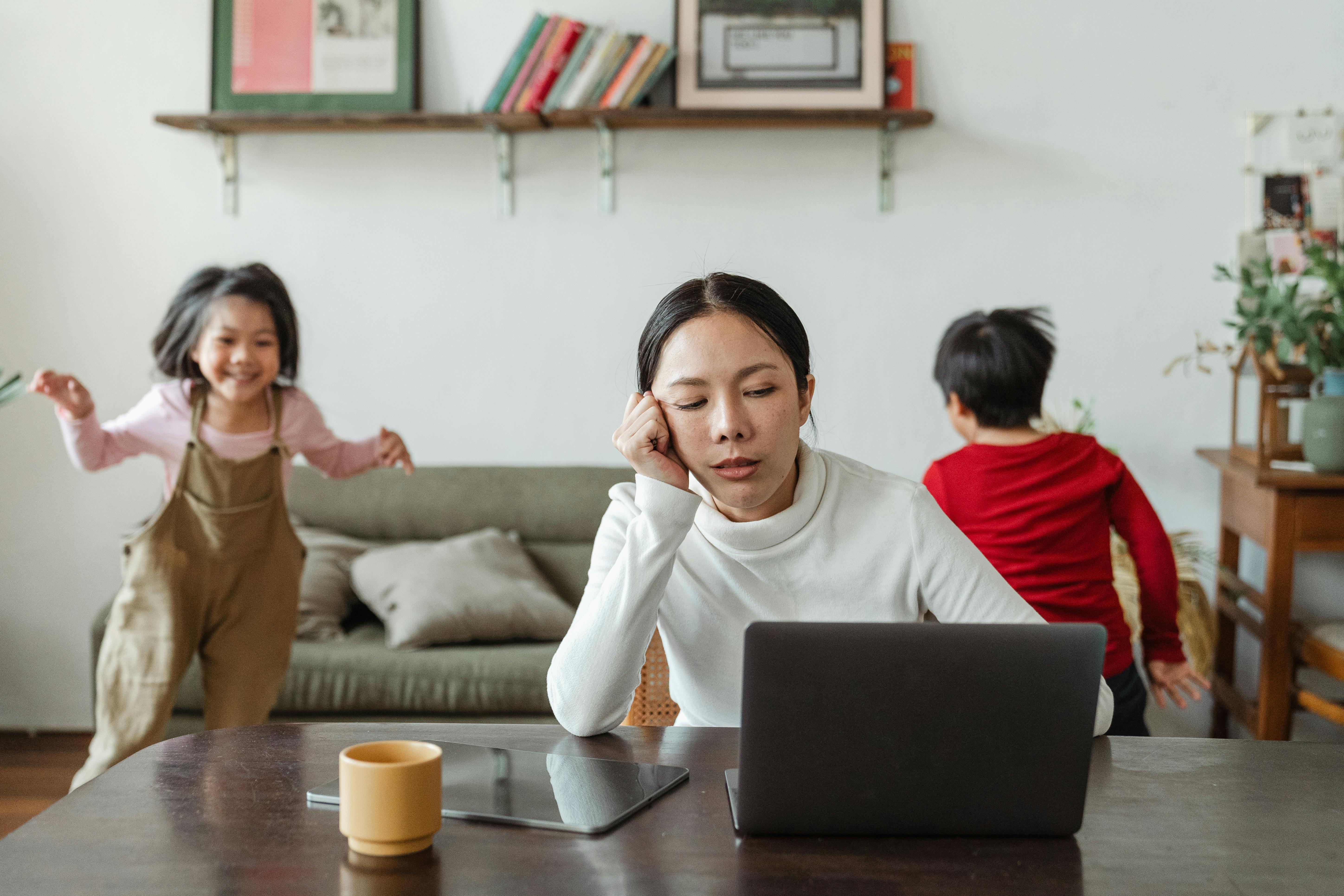 An exhausted woman sitting by a computer as her children play in the background | Source: Pexels