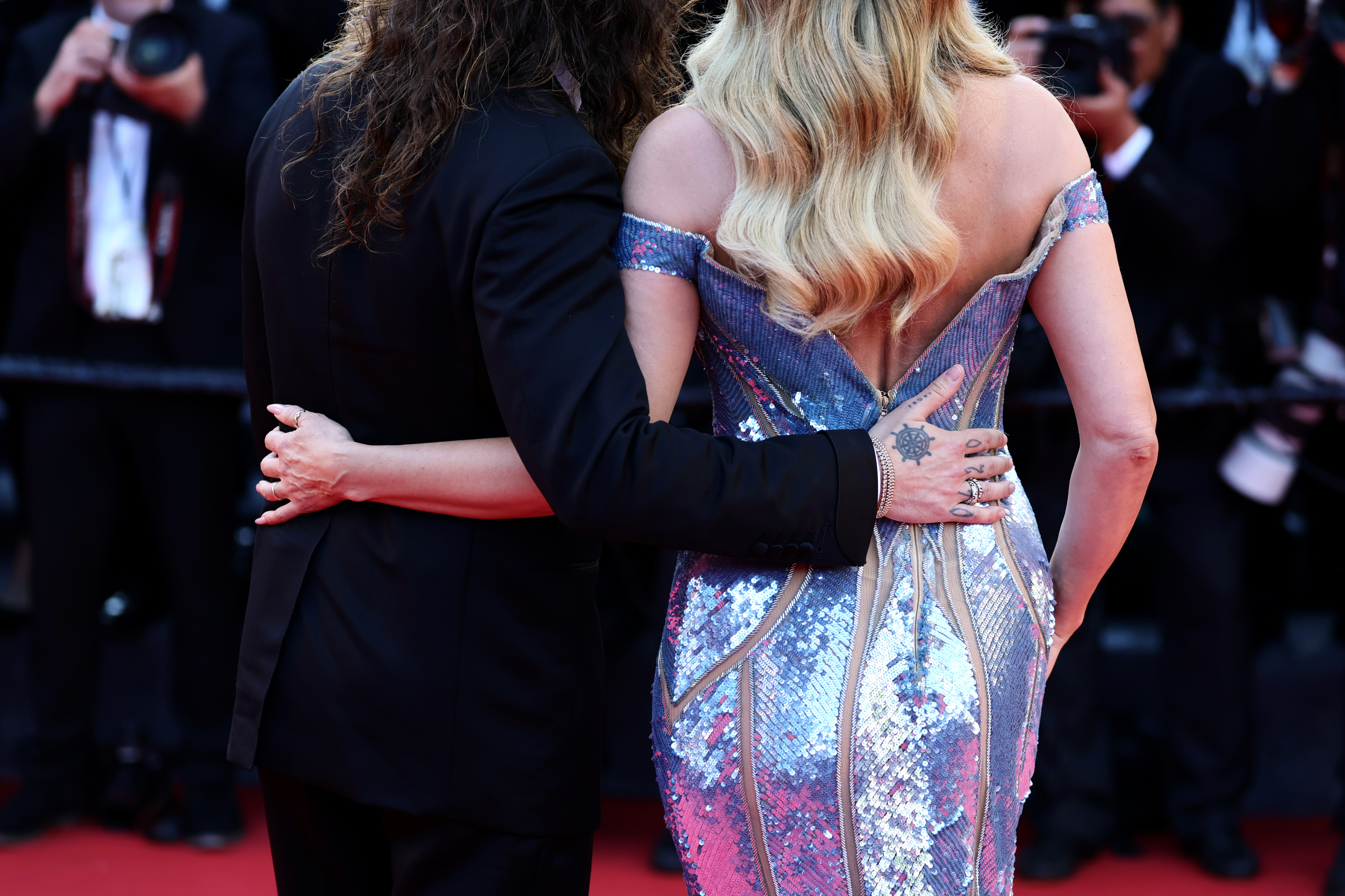Photographed from behind, the couple rests their hands on each other's waists. The gown's daring plunge mirrors at the back, stopping just before a sleek zipper — a clever flourish that shows off the dress's masterful design.