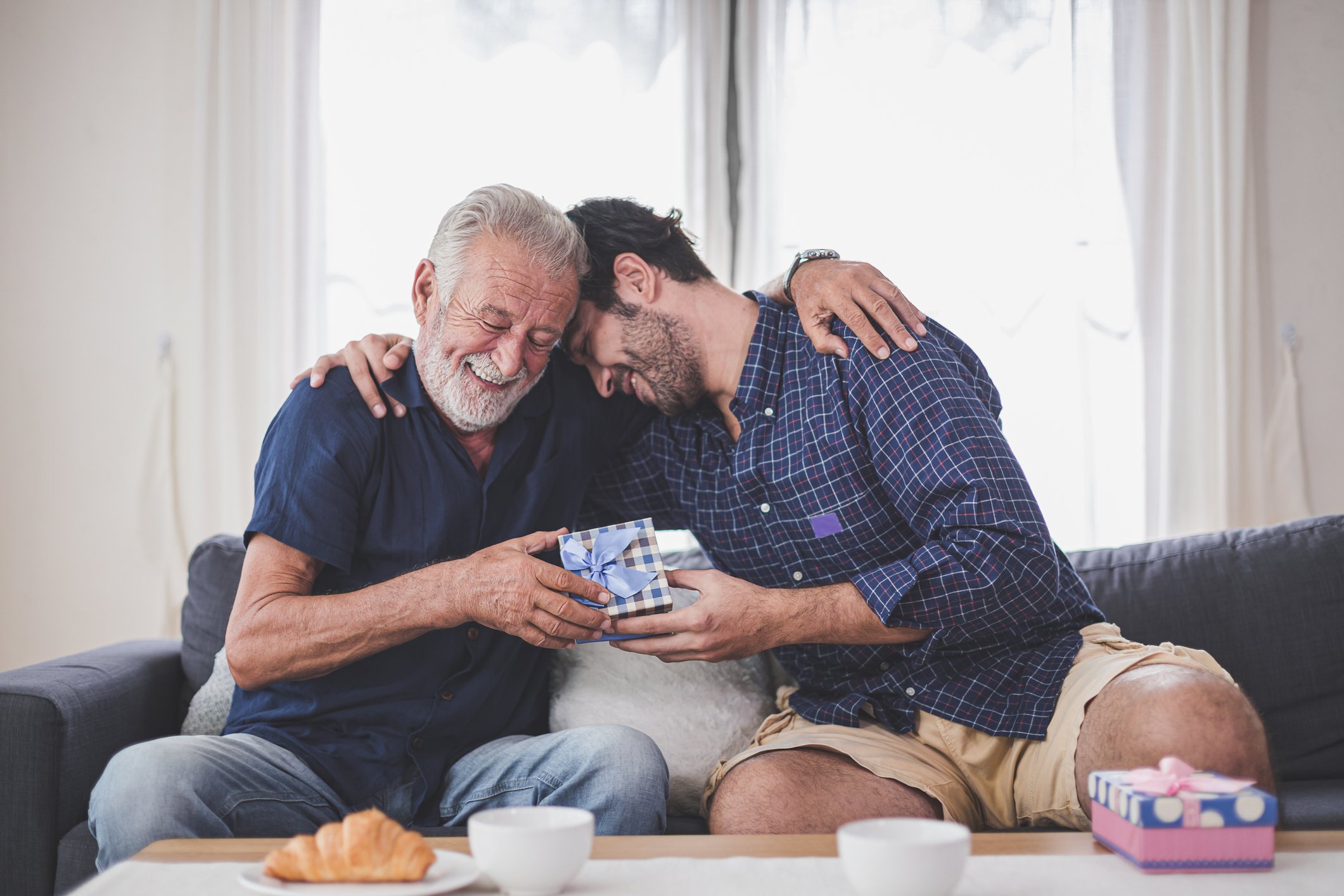 Sohn, der Vater ein Geschenk gibt, während er zu Hause auf dem Sofa sitzt | Quelle: Getty Images