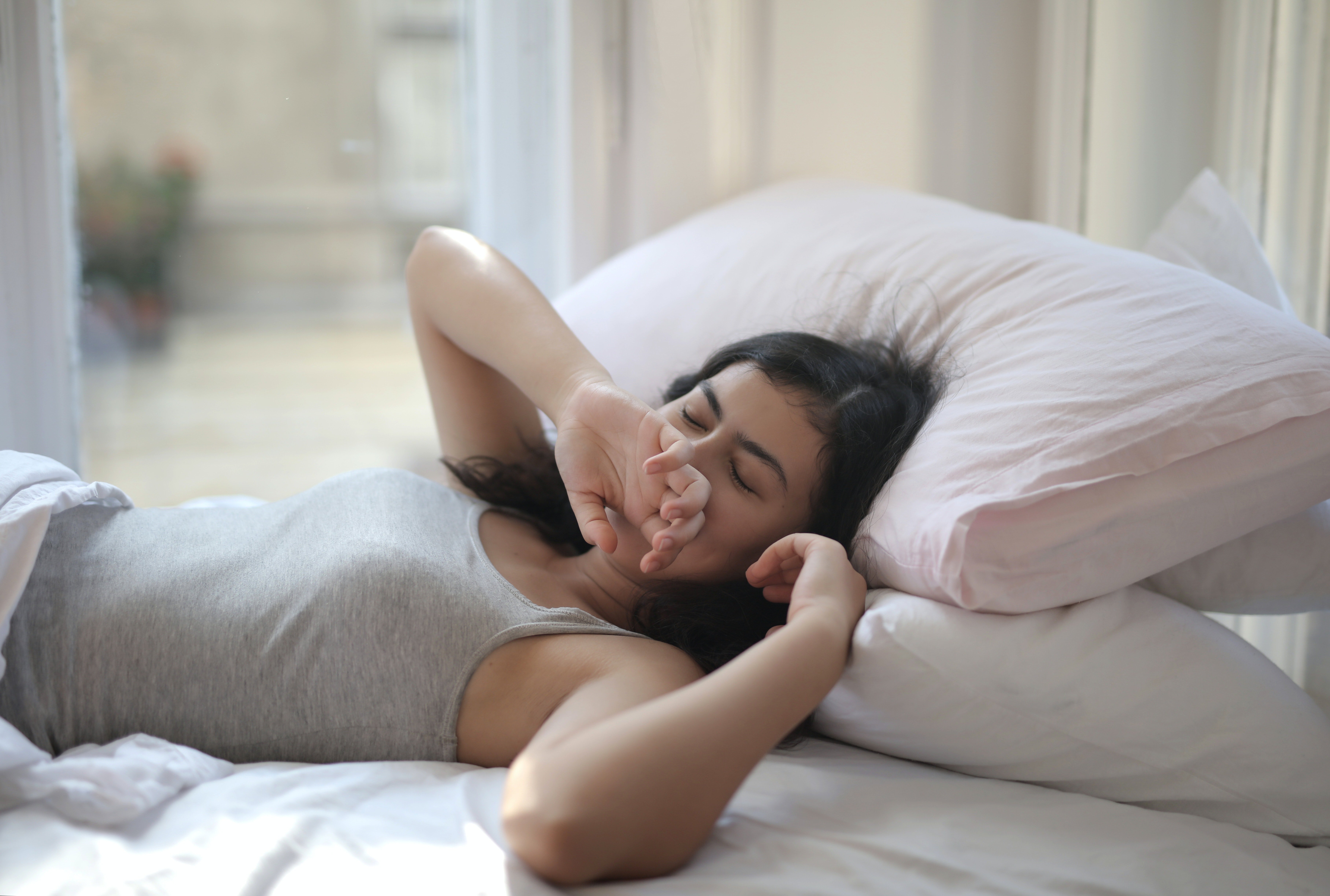 Verschlafene Frau in grauem Tanktop auf dem Bett liegend | Quelle: Pexels
