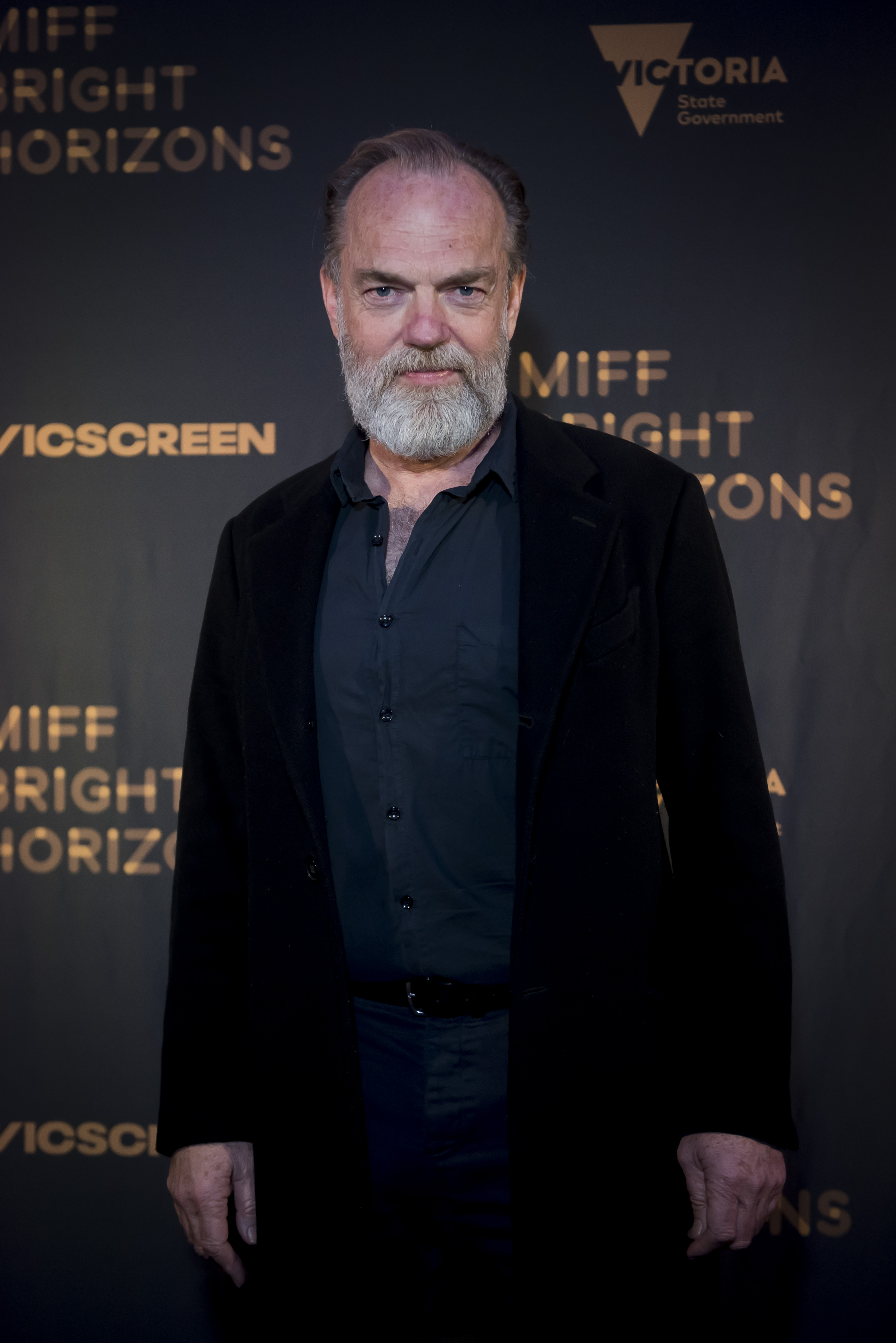 On August 5, 2023, Hugo Weaving attended the world premiere of "The Rooster" at the Melbourne International Film Festival (MIFF) in Australia, wearing an open-collared shirt and dark jacket. With a full silver beard and steady expression, Weaving carried a grounded presence — far from the elven halls of Rivendell, yet unmistakably regal.