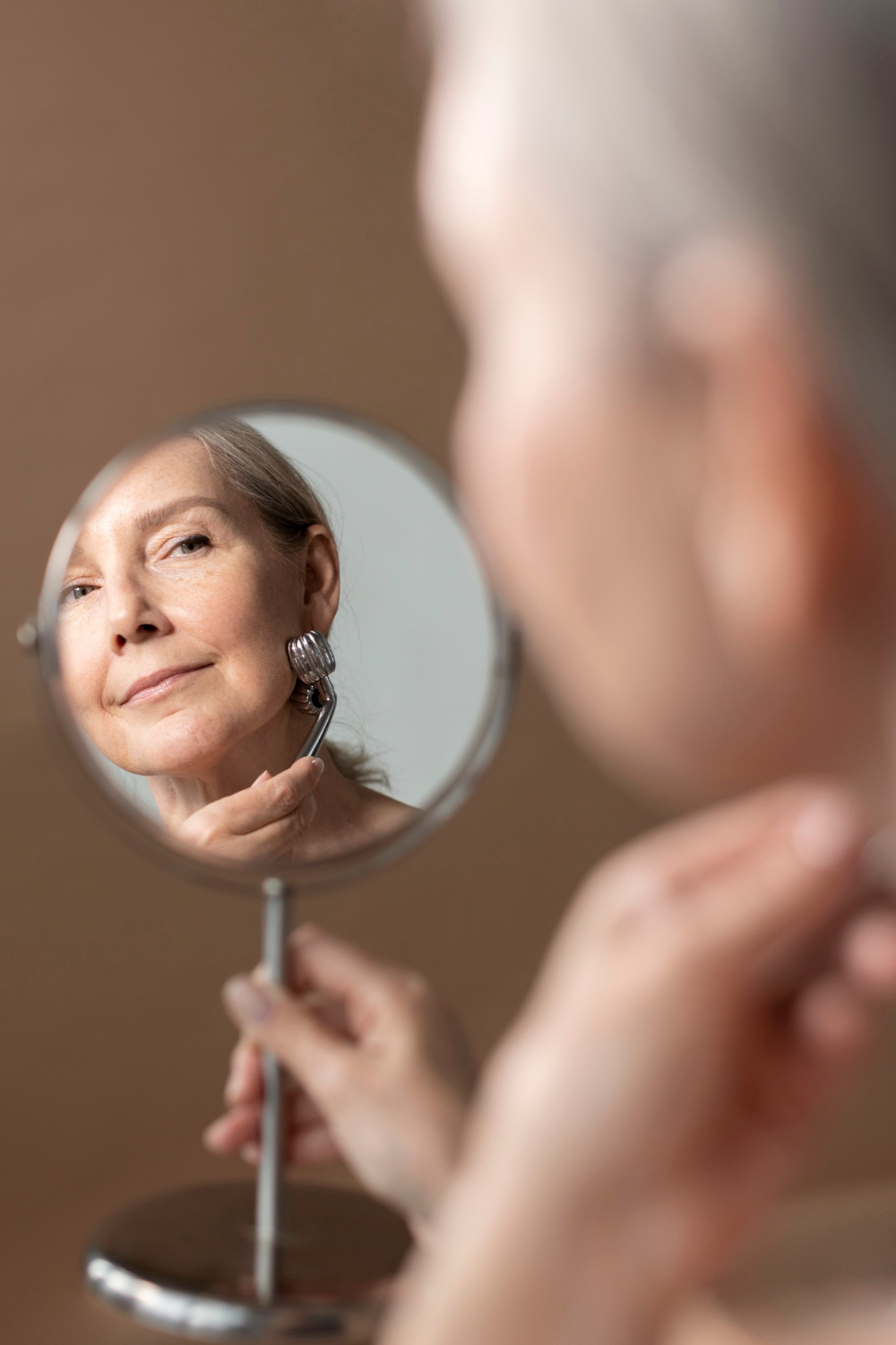 A senior woman looking in the mirror | Source: Freepik