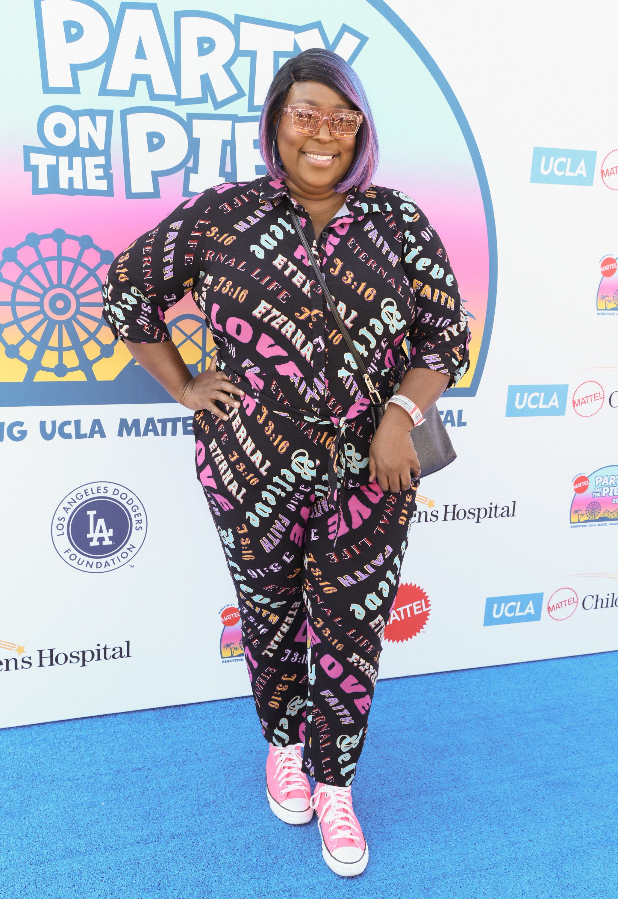 Loni Love attends the UCLA Mattel Children’s Hospital's Party on the Pier on November 5, wearing a colorful patterned outfit, pink sneakers, and tinted glasses on the blue carpet.