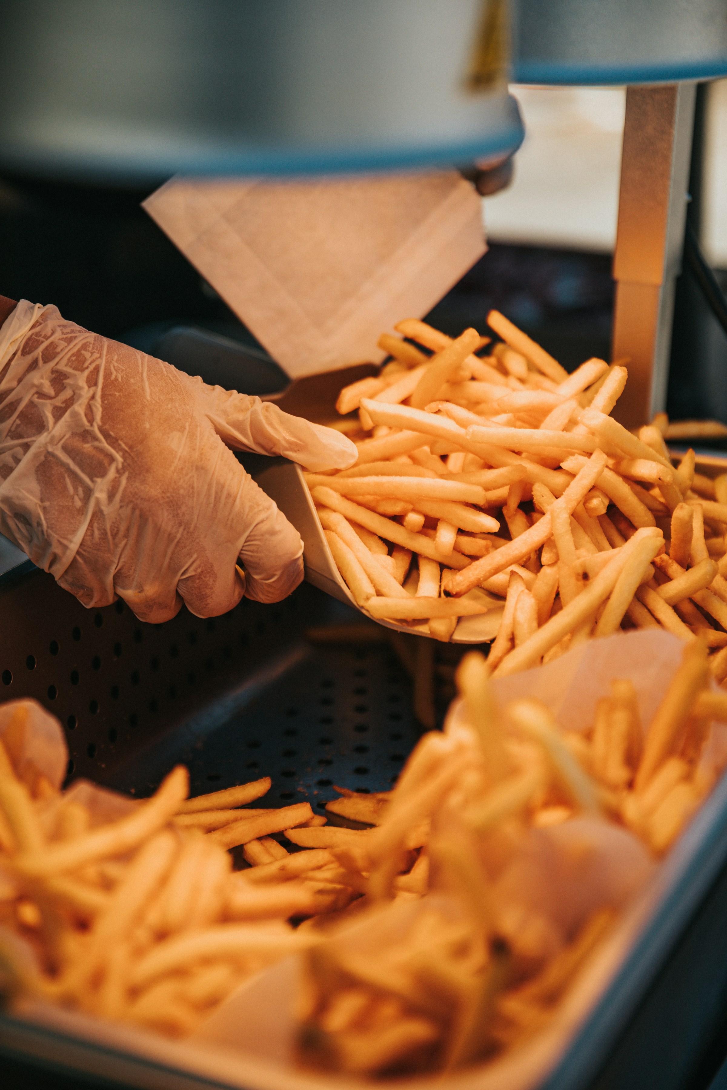 A person with a gloved hand scooping French fries from a tray | Source: Unsplash