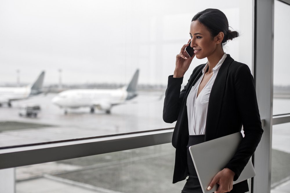 Mujer hablando por teléfono usando un blazer negro y falta negra sosteniendo una portátil. | Foto: Shutterstock Mujer hablando por teléfono usando un blazer negro y falta negra sosteniendo una portátil. | Foto: Shutterstock