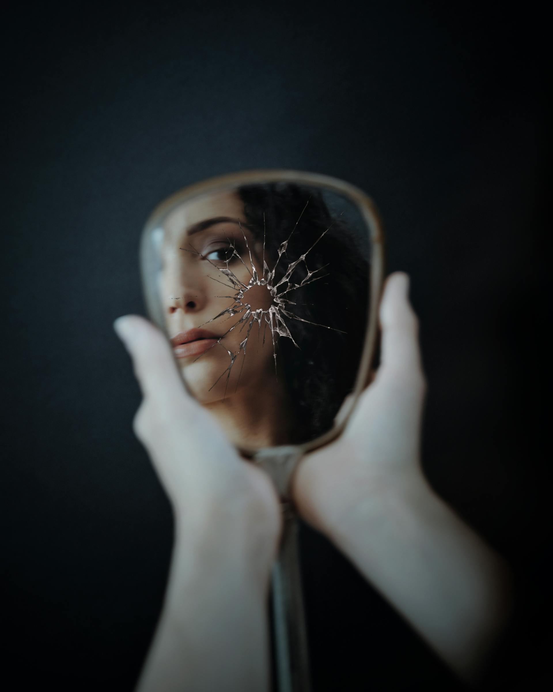 A woman looking at her reflection in a broken mirror | Source: Pexels