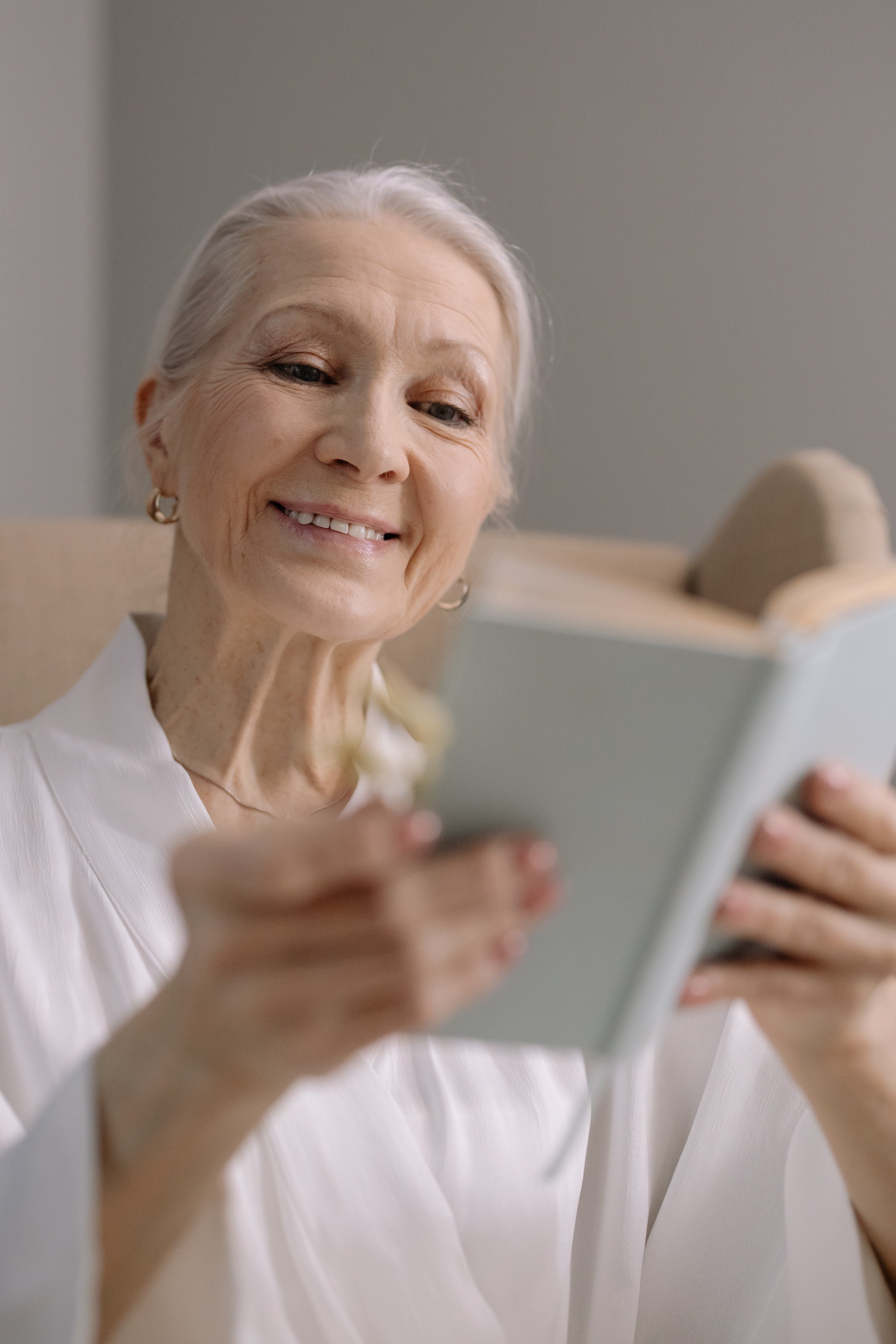 Anciana sonriendo feliz mientras lee un libro. | Foto: Pexels