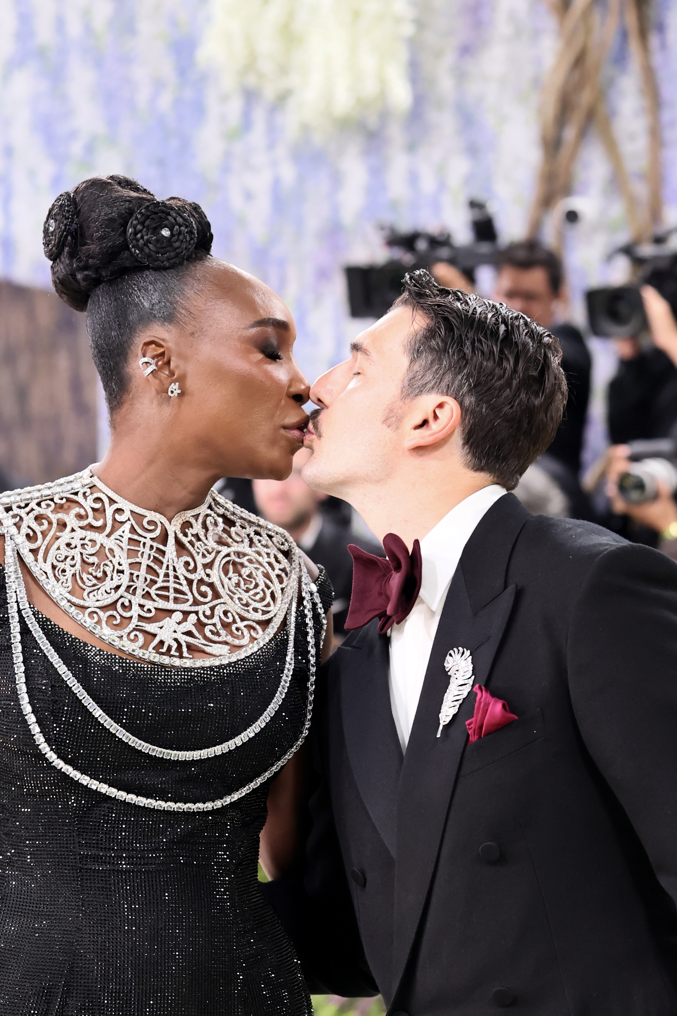 Venus Williams and Andrea Preti share a kiss at the 2026 Met Gala, with Williams in her embellished black gown and Preti in a tuxedo with a burgundy bow tie.