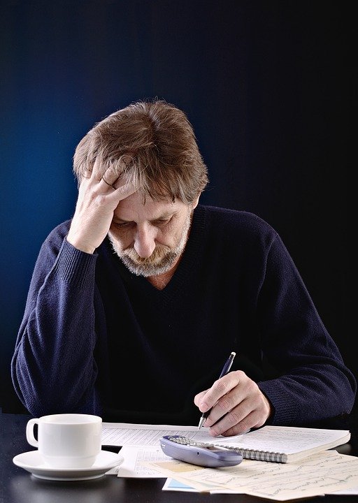 Hombre escribiendo en una hoja mientras posa su mano sobre su frente. | Foto: Pixabay