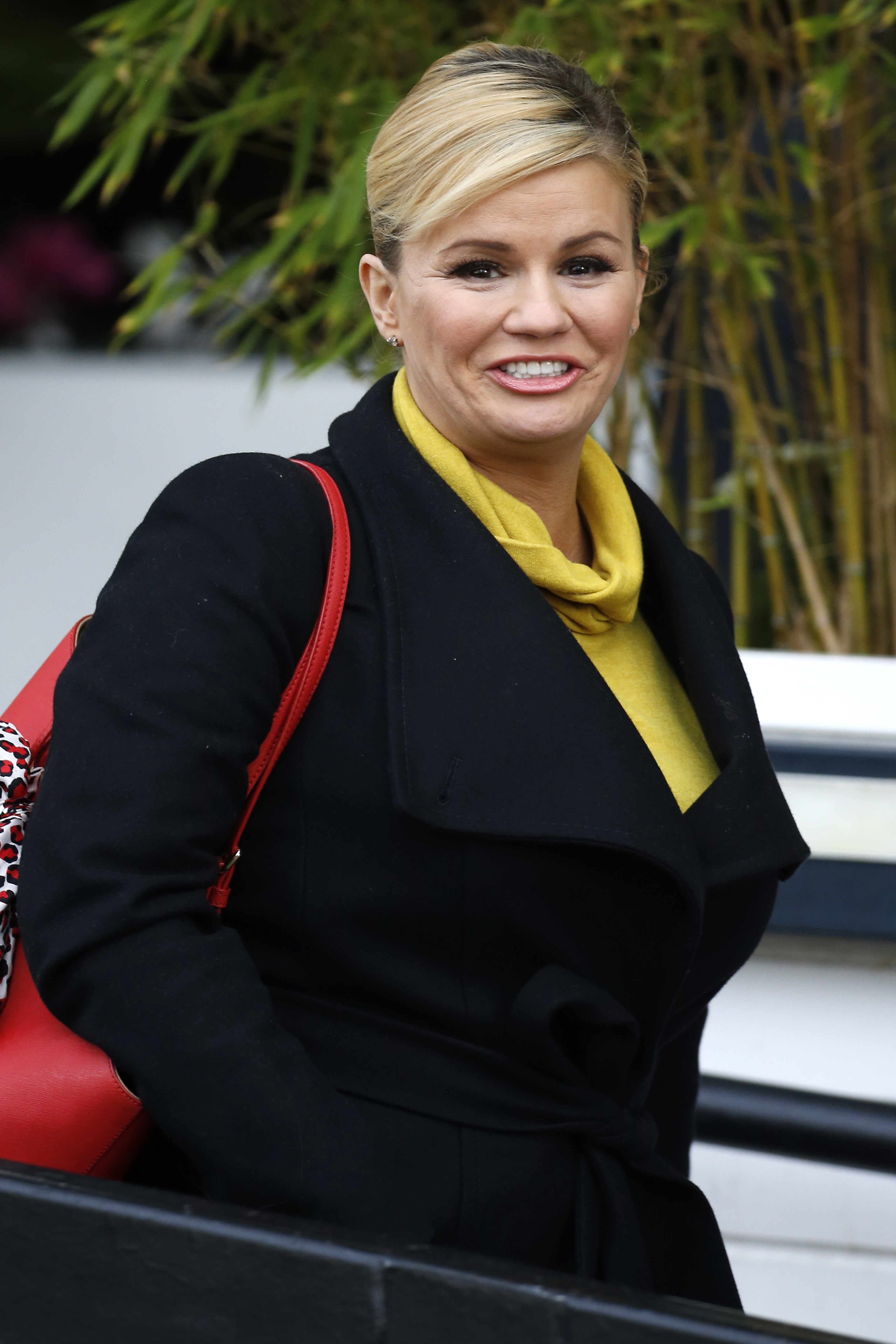Kerry Katona is seen leaving ITV Studios after appearing on Loose Women, wearing a black coat over a mustard top and smiling brightly as she carries a red handbag.
