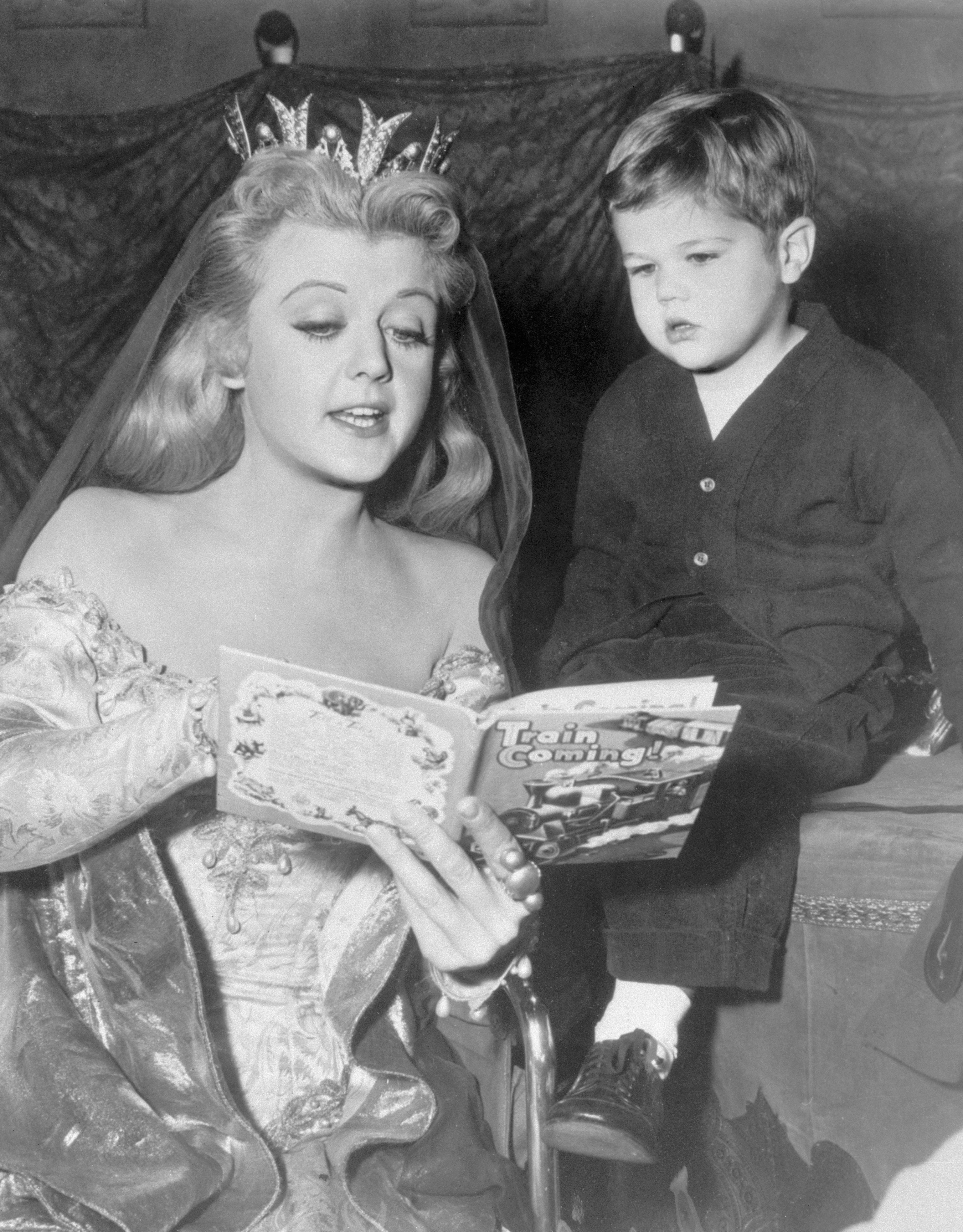 Angela Lansbury amuses a tiny visitor, her son, Michael, by reading a modern fairy tale during a break in Hollywood film work, 1955. | Source: Getty Images