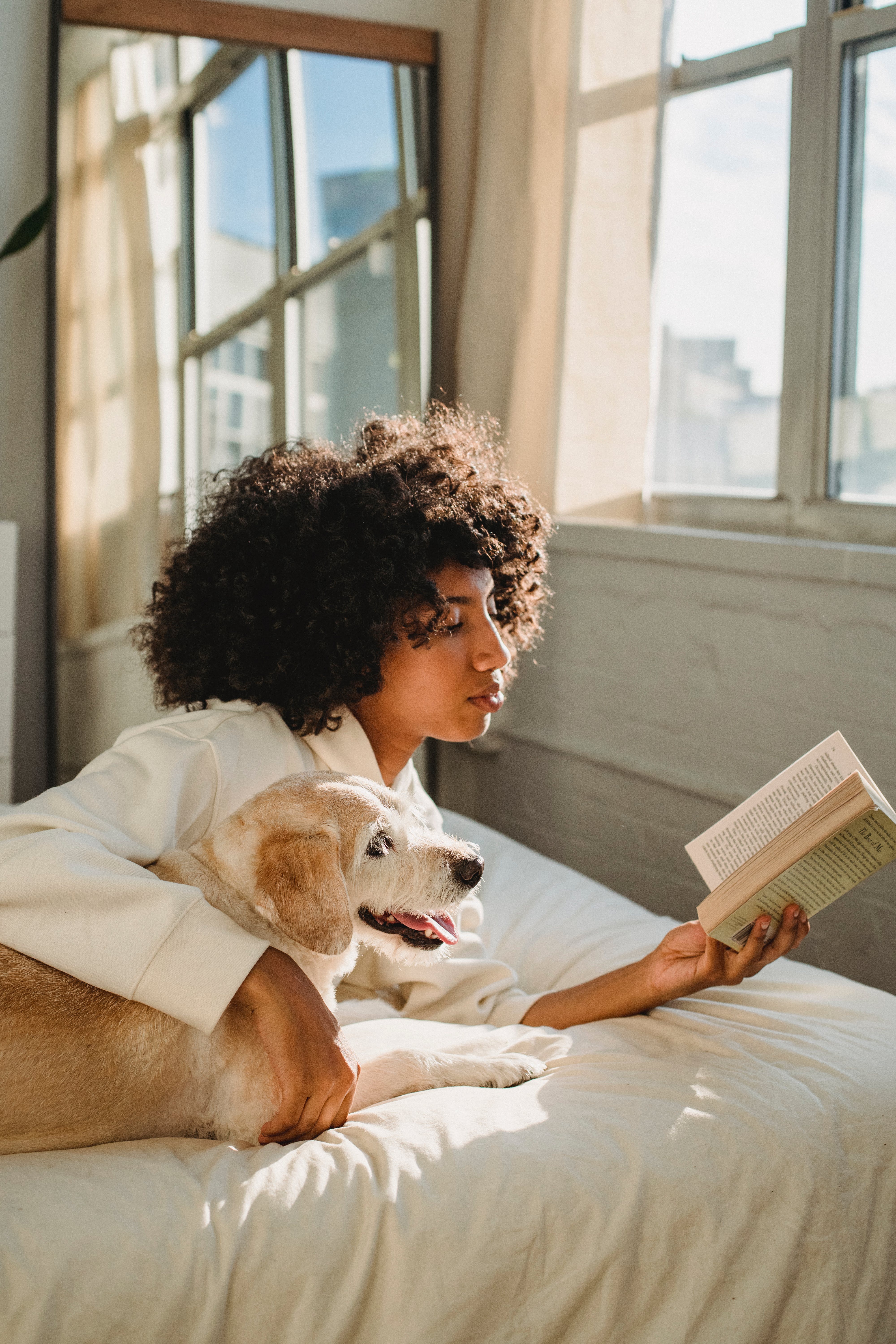 A young woman reading a book while cuddling her dog. | Source: Pexels