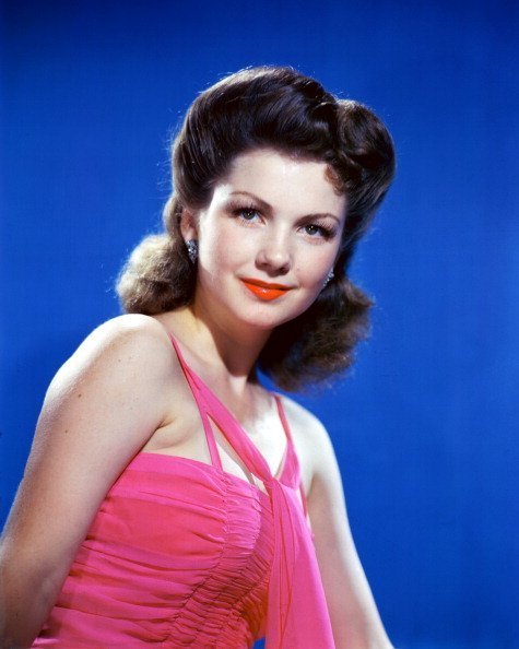 Anne Baxter (1923-1985), US actress, wearing a pink halterneck top in a studio portrait, against a blue background, circa 1945 | Photo: Getty Images