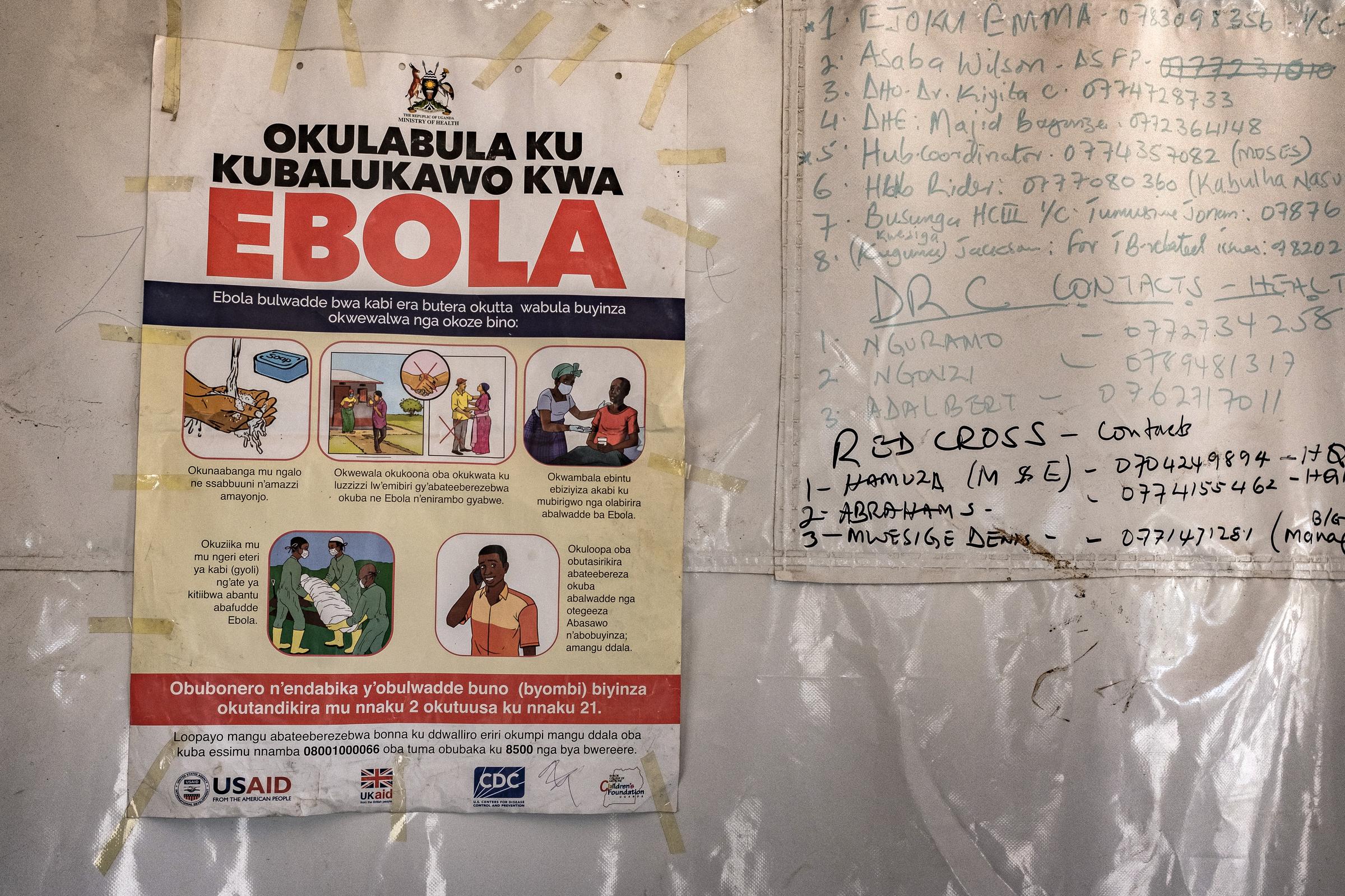 A poster displaying Ebola emergency contact numbers is pinned to a tent at the Busunga border crossing between Uganda and the Democratic Republic of Congo in Bundibugyo, on May 18, 2026. | Source: Getty Images