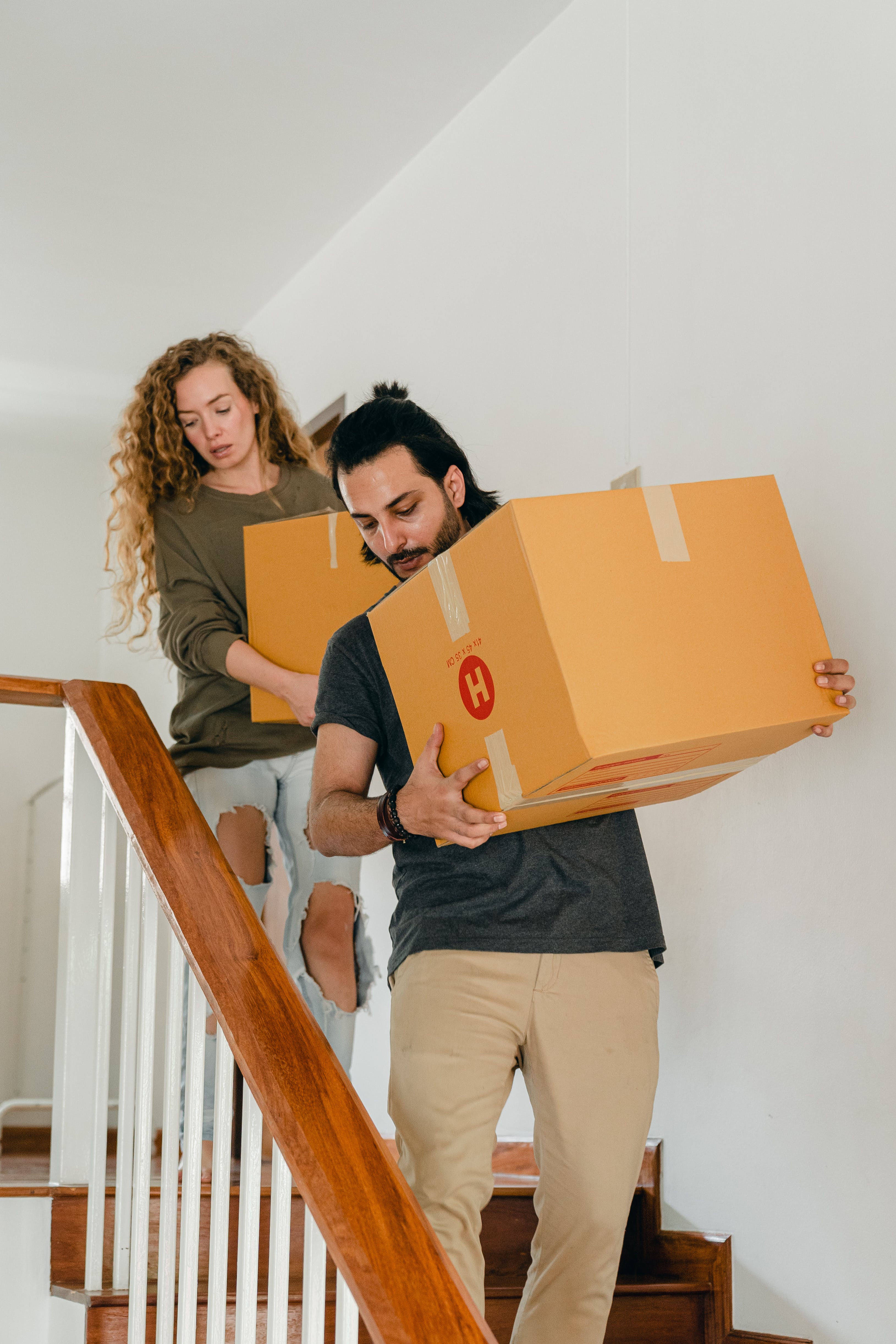 A young couple carrying boxes while walking down the stairs | Source: Pexels