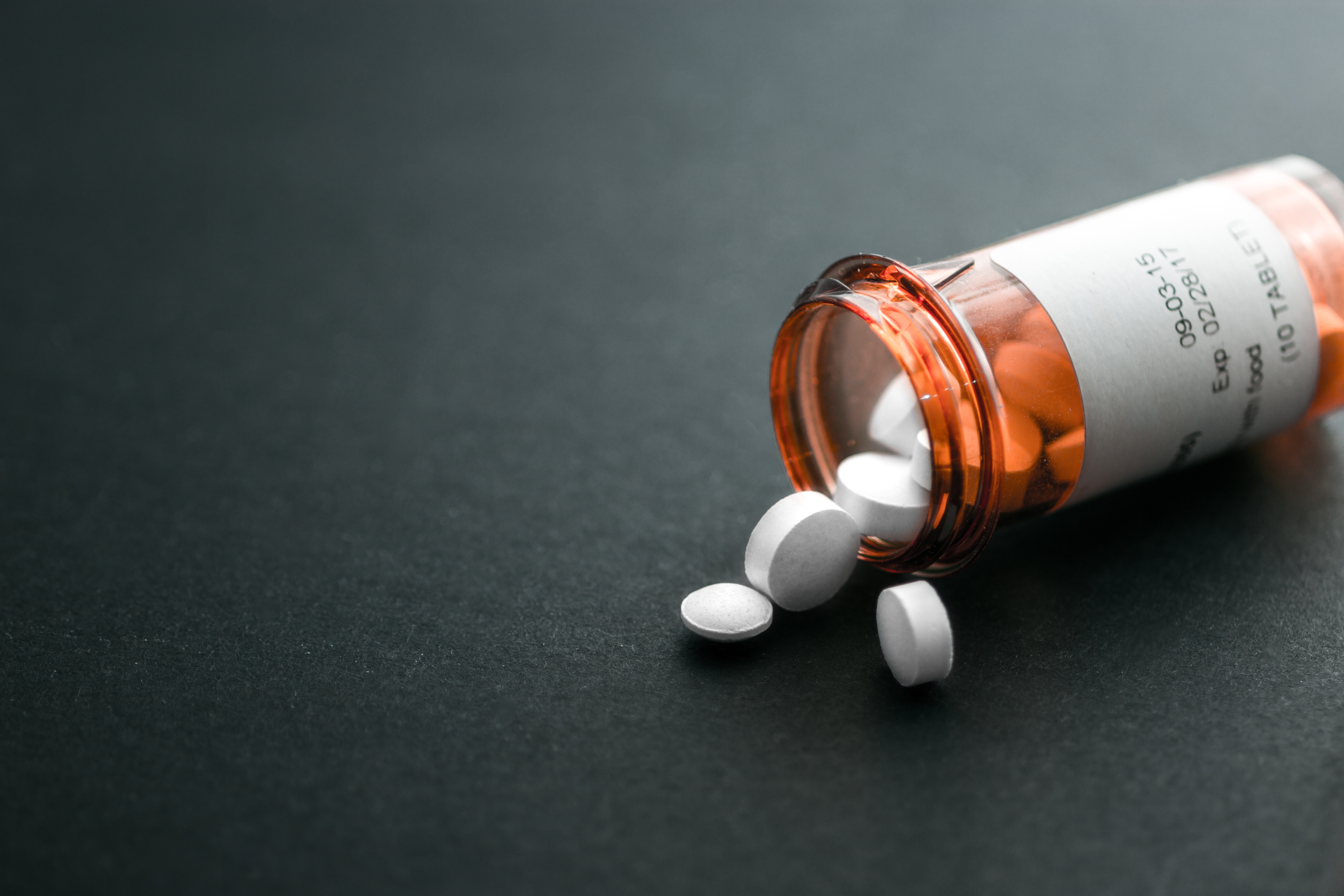 White pills spilling out of a toppled bright red orange pill bottle. | Source: Shutterstock