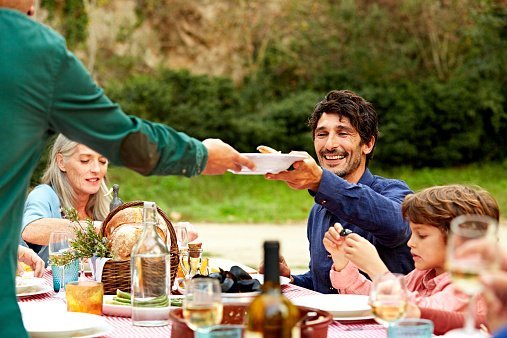 Men passing dish while having meal with family at outdoor table in yard | Photo: Getty Images