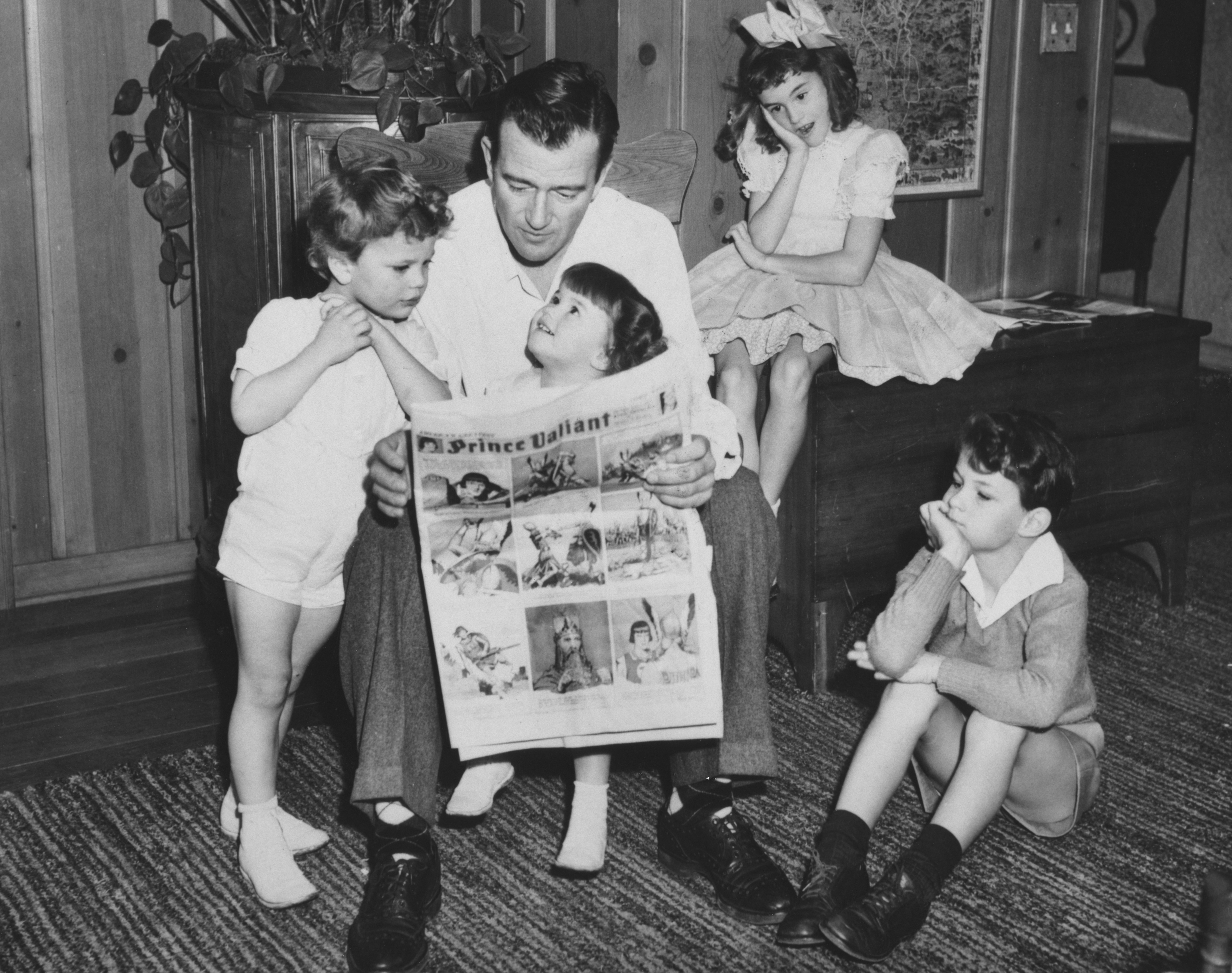 John Wayne reading with his sons Michael and Patrick Wayne, and his daughters Melinda andToni Wayne at their family home in Encino, California, circa 1943. | Source: Getty Images