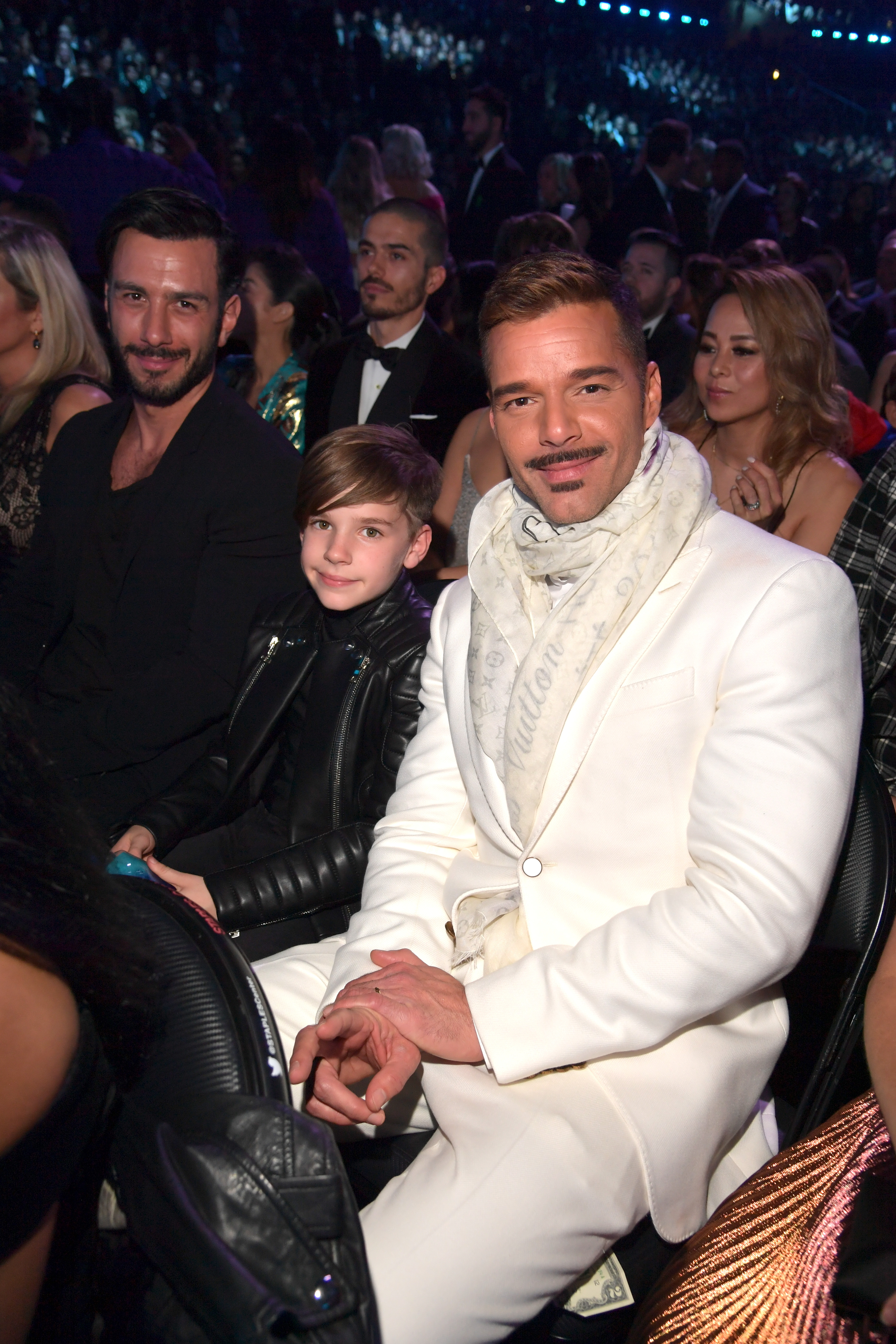 Ricky Martin sits beside one of his twin sons and Jwan Yosef at the 61st Annual Grammy Awards, wearing a white suit and scarf as the family poses from their audience seats.
