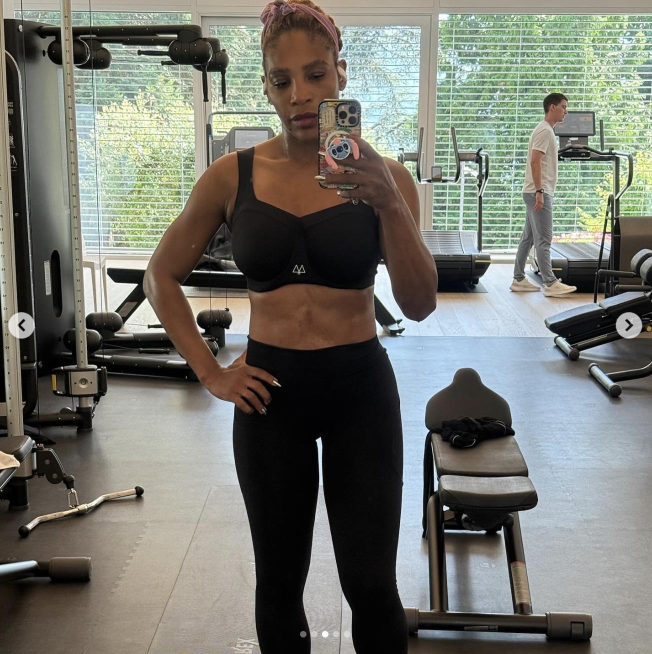 Standing tall with one hand on her hip, Serena Williams captured a clear view of her toned abs and arms. The gym setting behind her featured exercise machines, with natural light flooding through wide blinds.