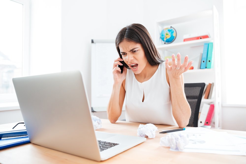 Angry businesswoman talking on the phone in office. | Photo: Shutterstock