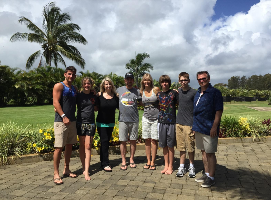 In a lush tropical setting, Chuck Norris stands surrounded by family, including Dina Norris DiCiolli, her husband Damien, and their boys, Dante and Eli. | Source: Facebook/ChuckNorris