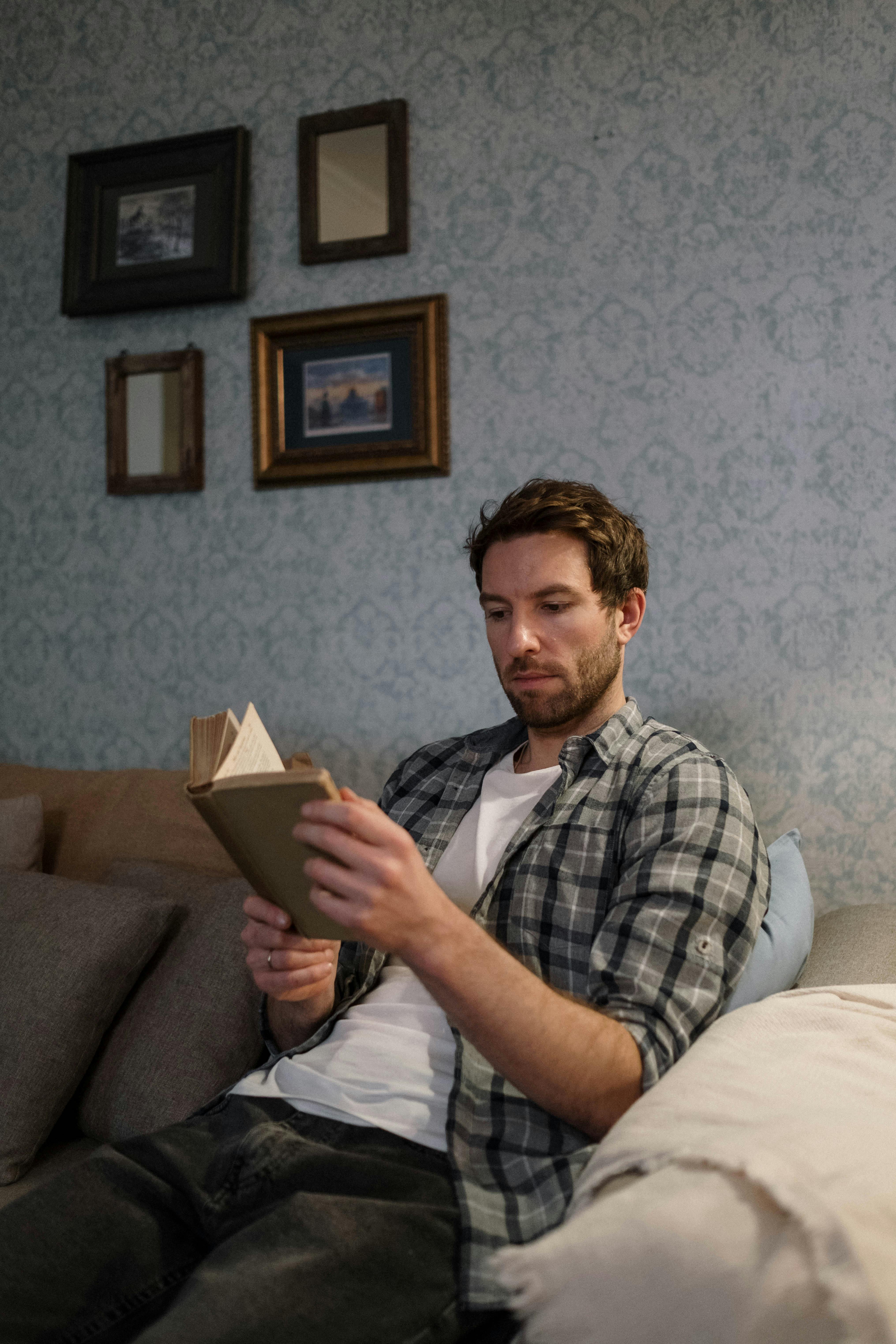 A man sitting on a couch, reading a book | Source: Pexels