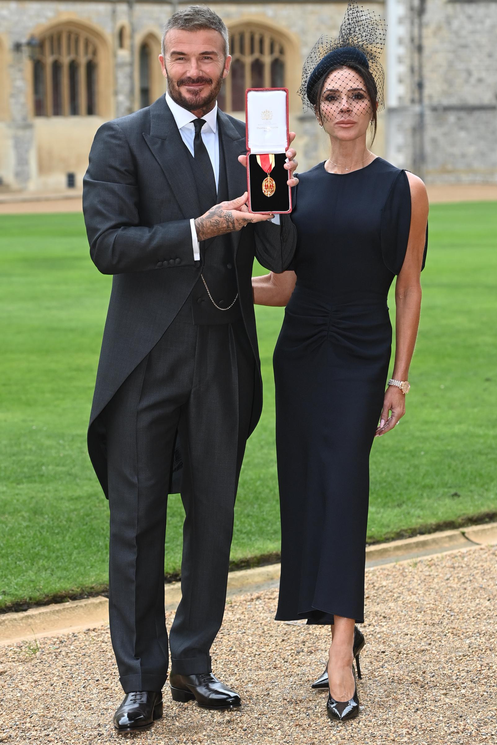 David Beckham holding up his medal as Victoria Beckham poses next to him during the investiture. | Source: Getty Images
