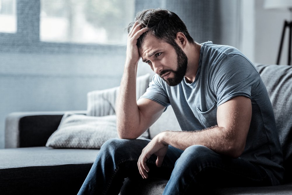 An unhappy man sitting on the sofa and holding his forehead. | Photo: Shutterstock.