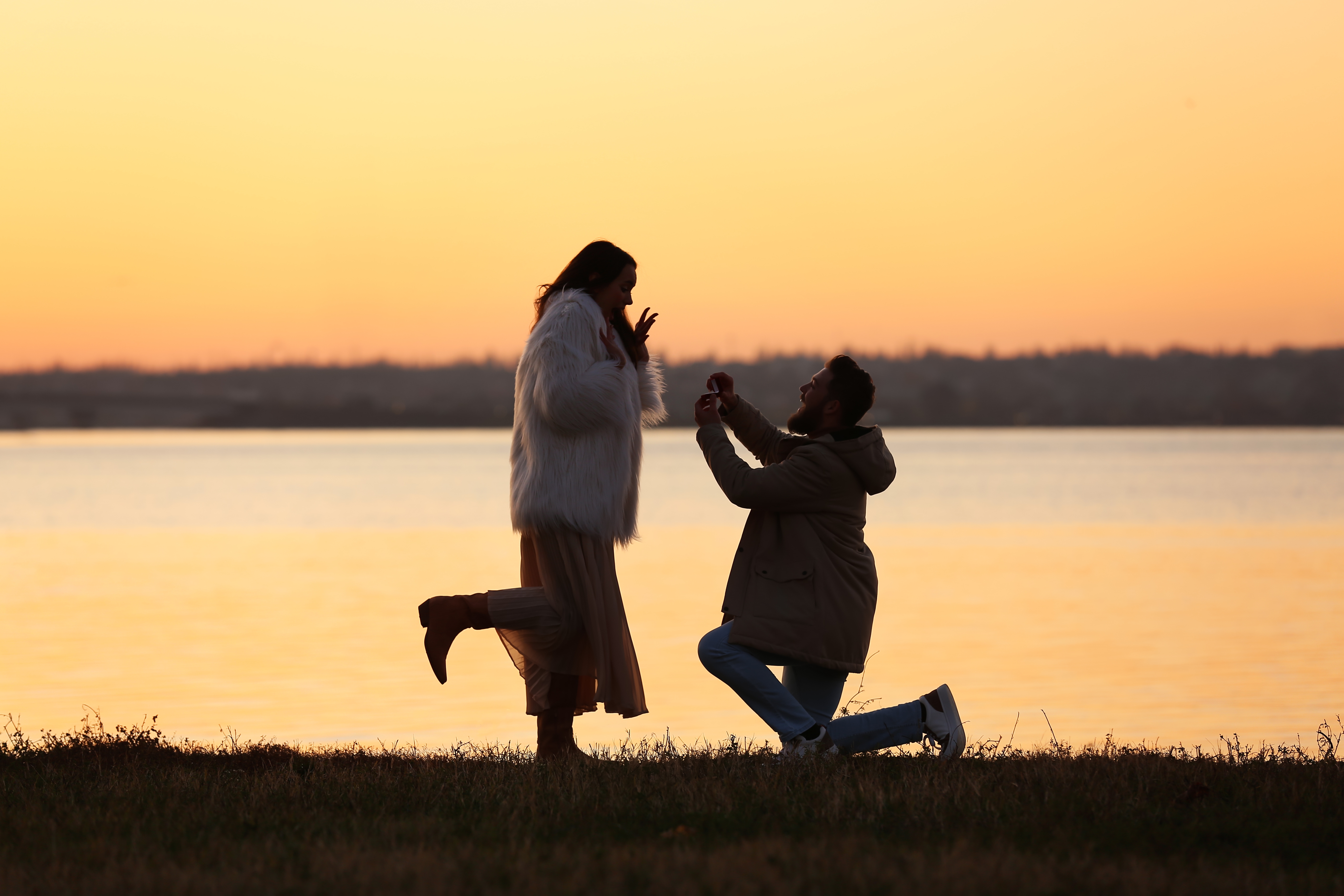 Young man proposing to his girlfriend near river at sunset. | Source: Shutterstock
