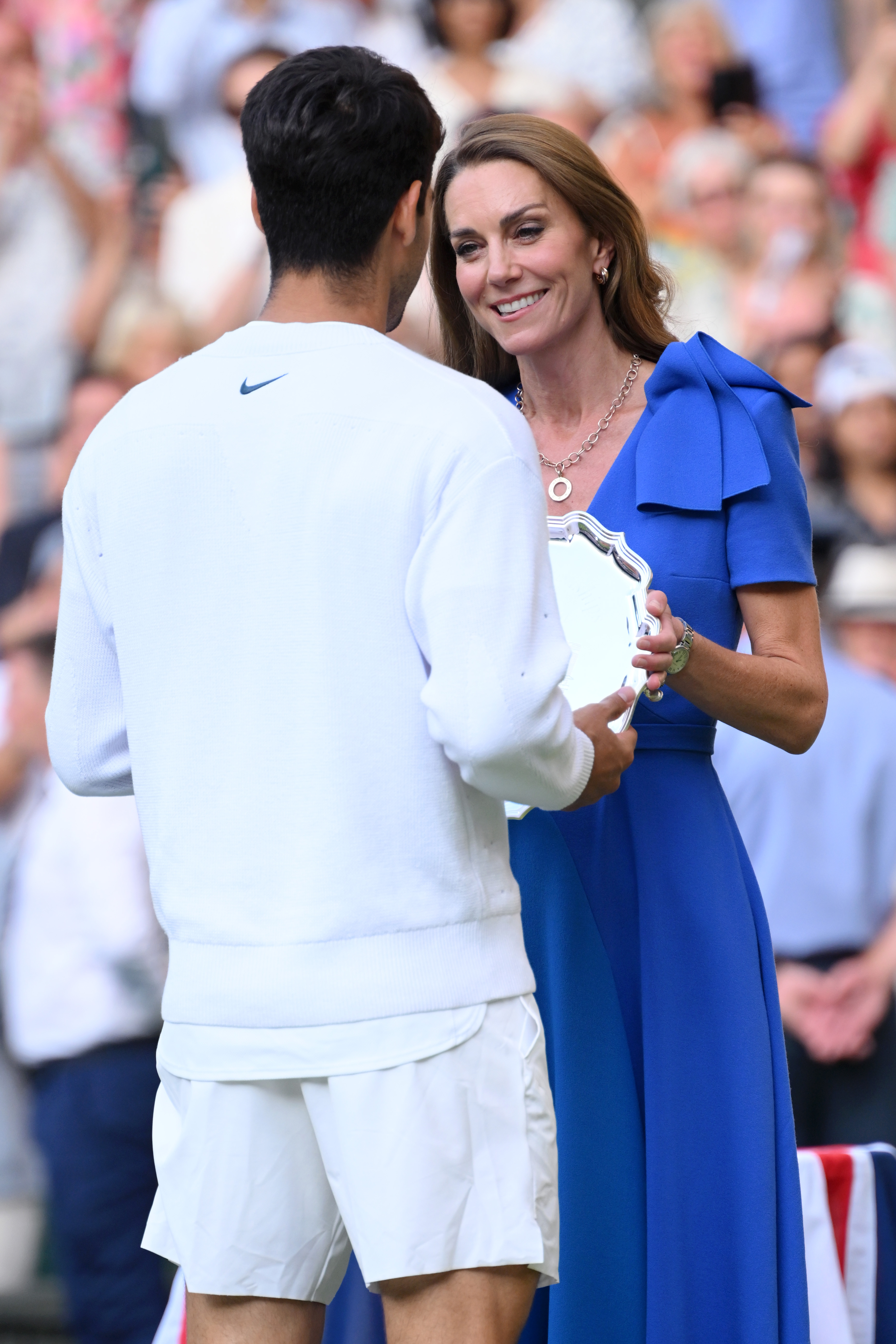 Princess Catherine hands the runner-up trophy to Carlos Alcaraz during the Wimbledon award ceremony. She offers a gentle smile as he receives the silver plate.