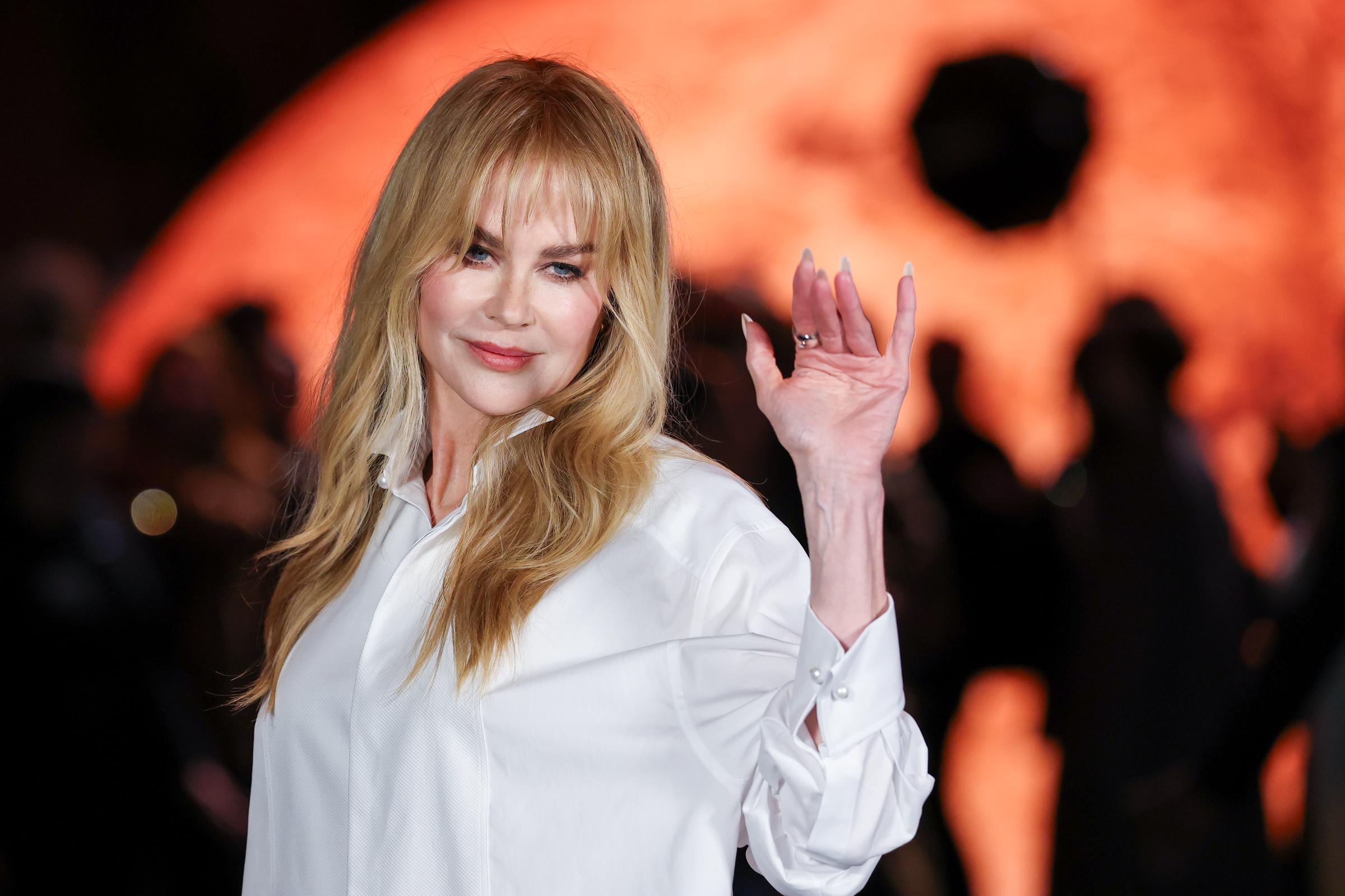With a graceful wave, Nicole Kidman captivates photographers. Her tousled hair and curtain bangs command attention against the fiery planet-like backdrop, closing out a powerful post-divorce fashion moment.