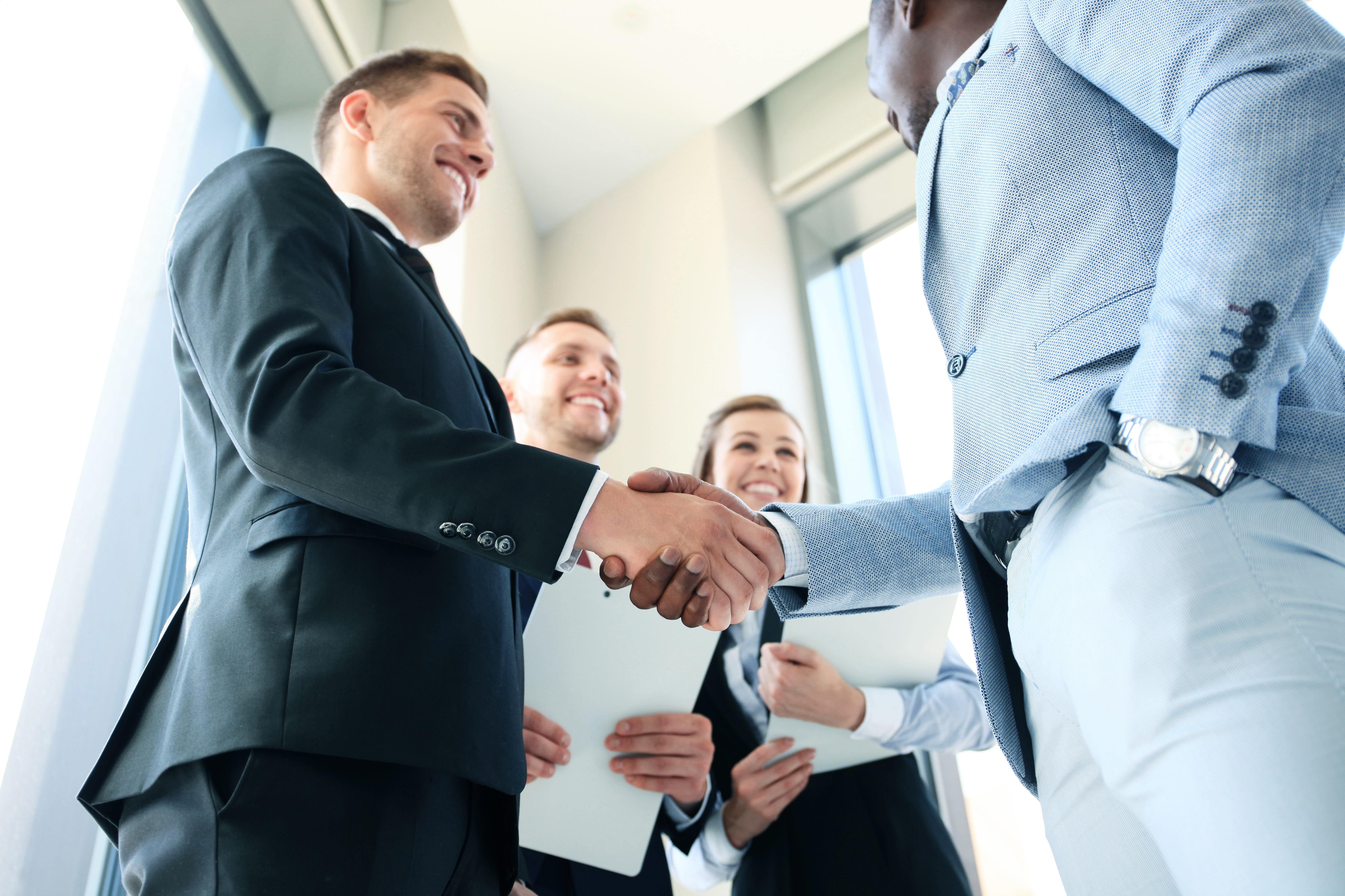 Two men in suits shaking hands as two other colleagues smile beside them | Source: Shutterstock