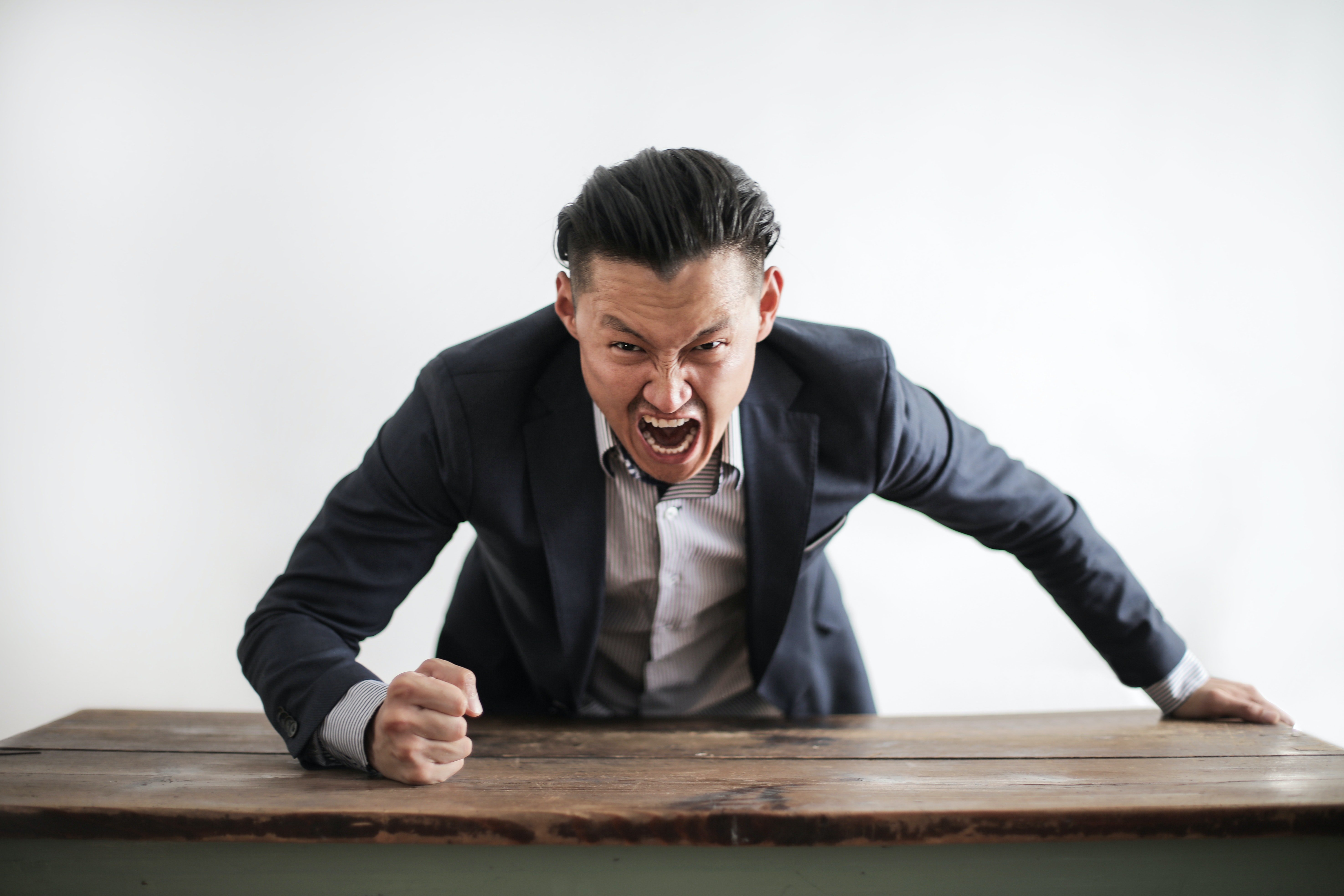 An angry man pounding his clenched fist on a table. | Photo: Pexels