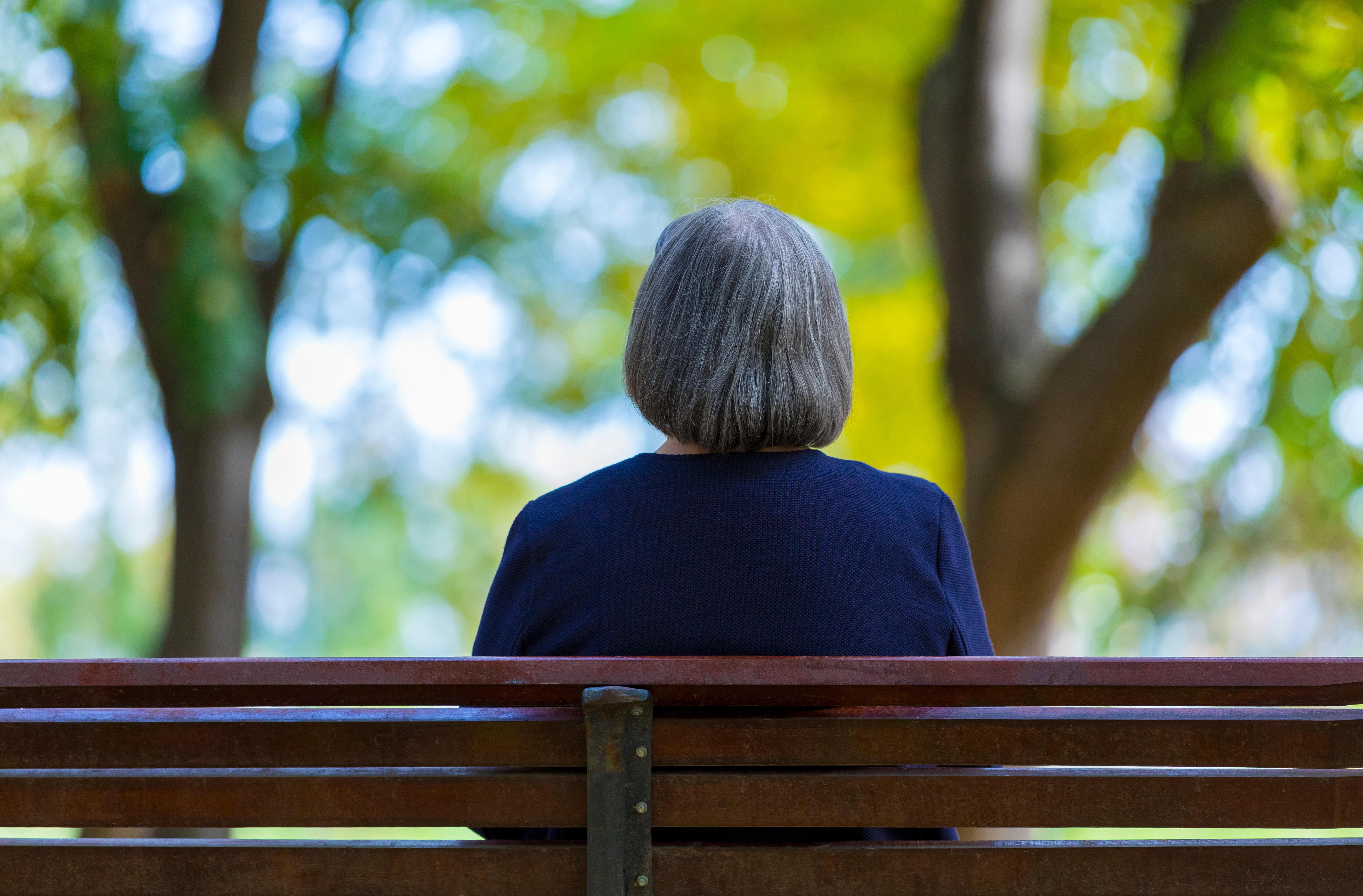 A back view of a senior woman sitting alone on a bench outside | Source: Shutterstock